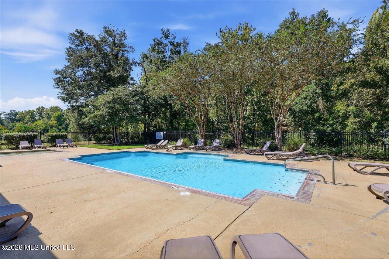 Outdoor swimming pool surrounded by lounge chairs, trees, and a black metal fence.