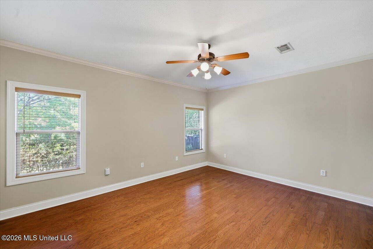 Empty room with hardwood floors, two windows, and a ceiling fan.