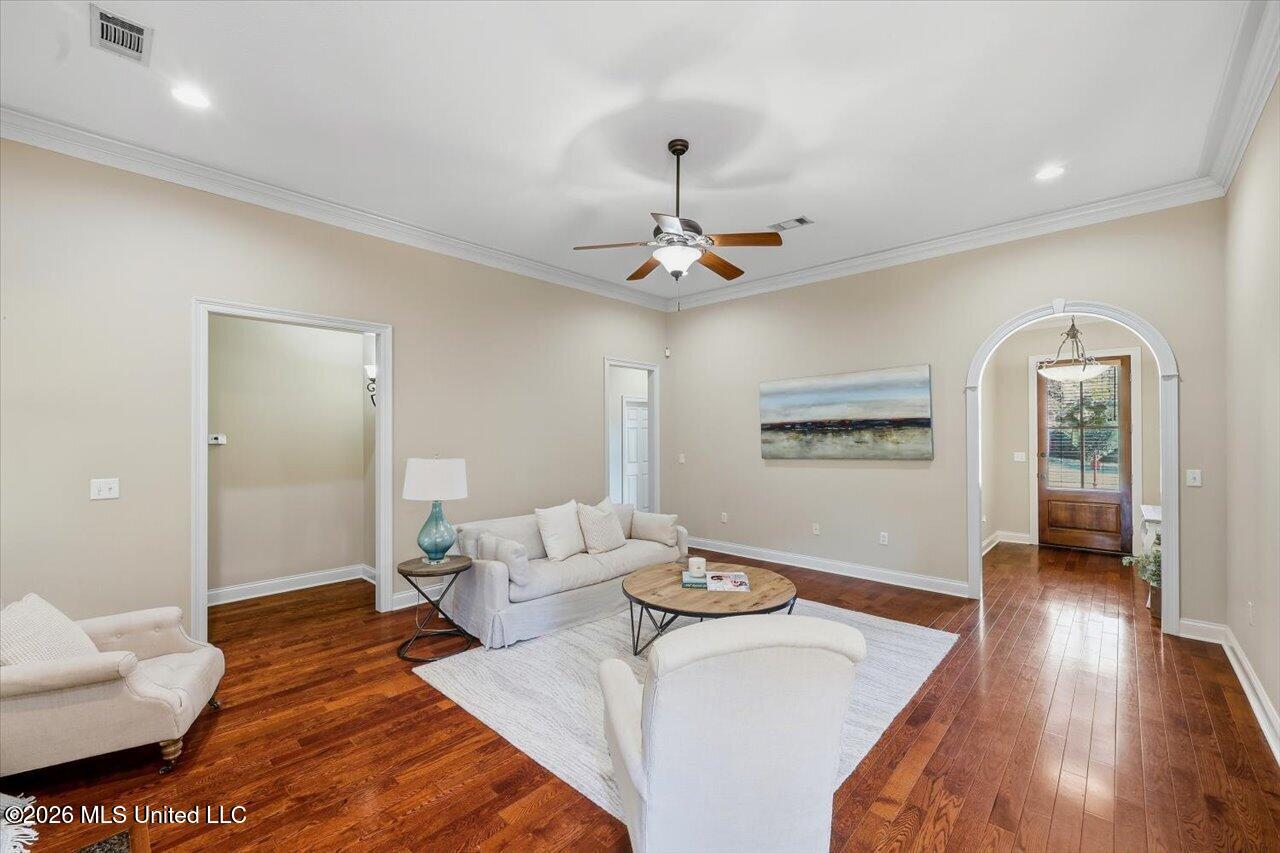 Living room with hardwood floors, cream seating, a ceiling fan, and arched doorway.