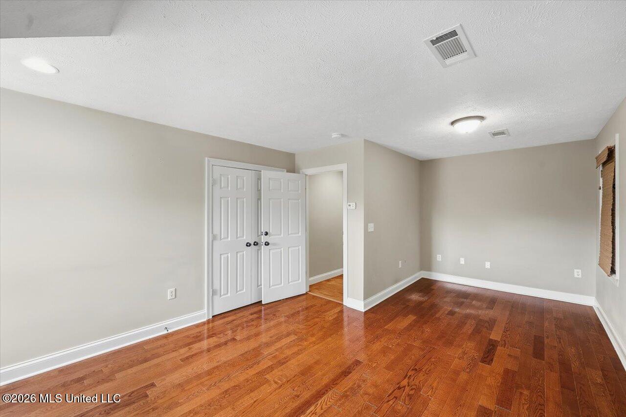 Empty room with polished hardwood floors, beige walls, and white double doors.