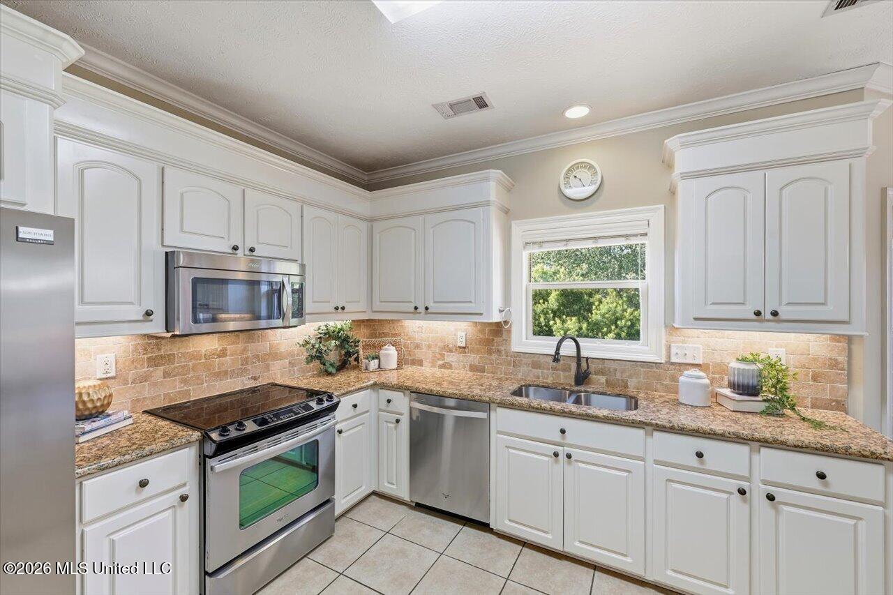 Kitchen with white cabinets, granite counters, stainless steel appliances, and a double-basin sink beneath a window.
