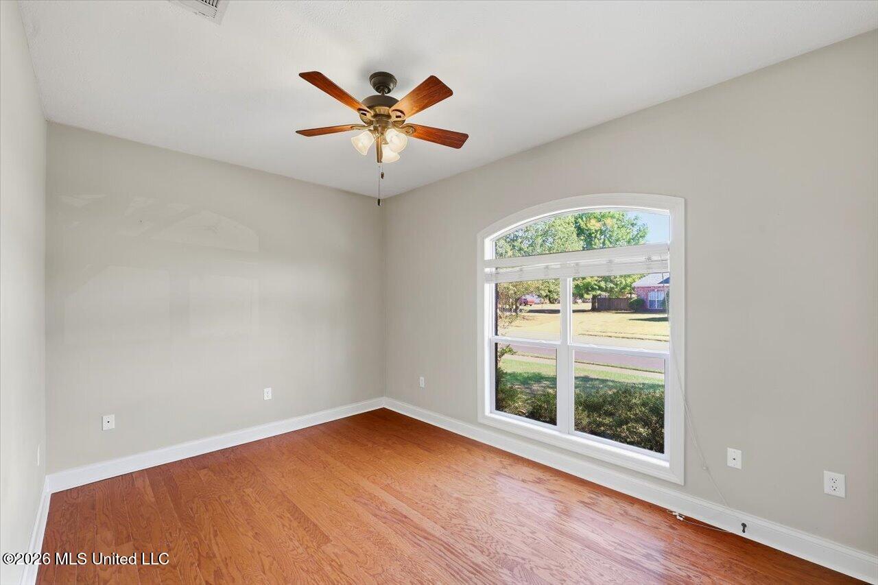 Empty room with hardwood floors, a ceiling fan, and a large arched window.