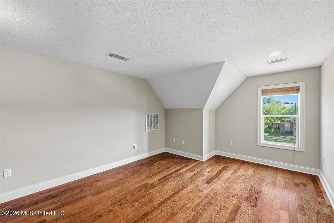 Empty room with hardwood floors, a window, and an angled ceiling.