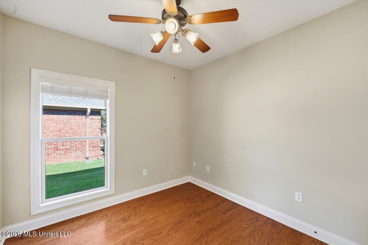 Empty room with hardwood floors, a ceiling fan, and a large window.
