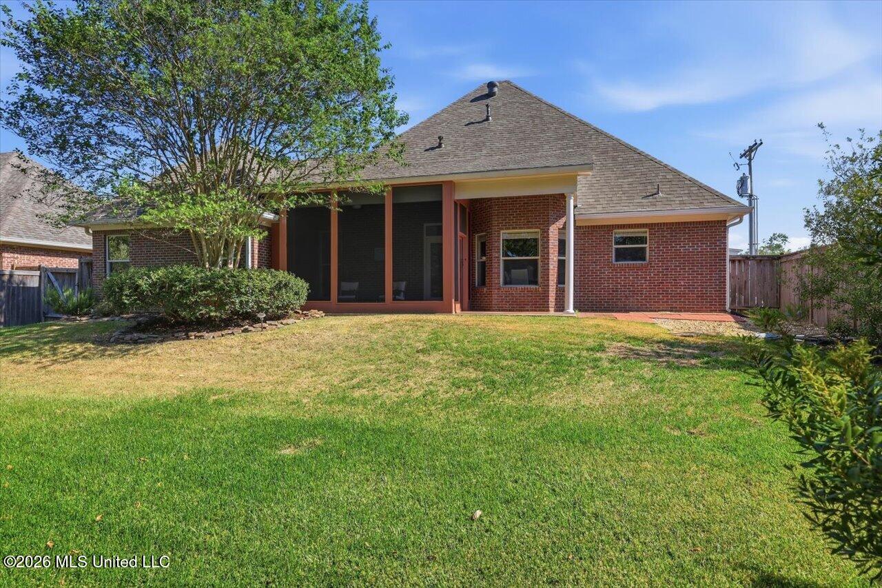 Rear exterior of a brick home with a screened porch and broad lawn.