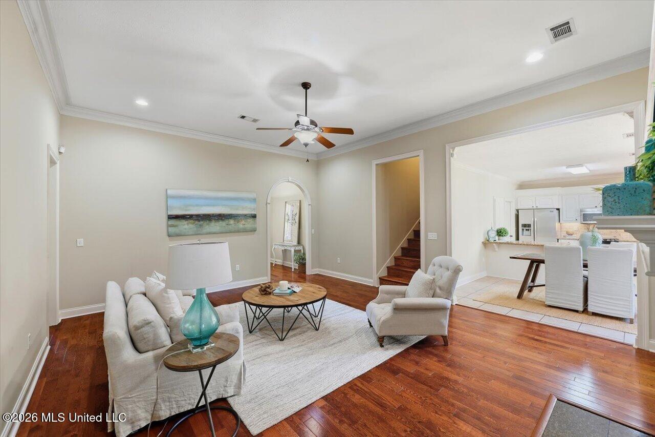 Staged living room with hardwood floors, ceiling fan, and open connection to kitchen.