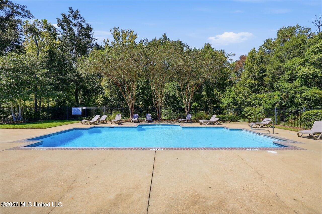 Outdoor swimming pool bordered by lounge chairs, trees, and a black metal fence.