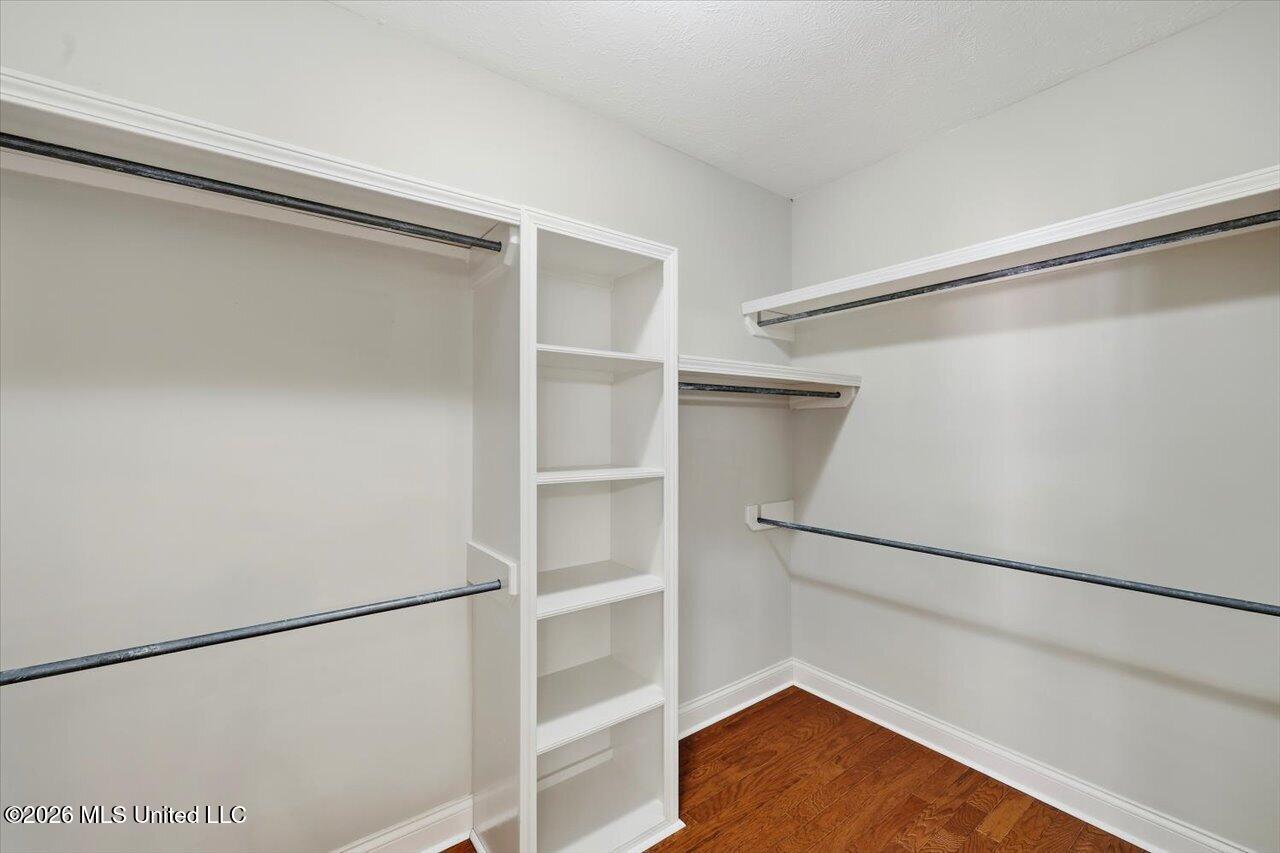 Walk-in closet with built-in shelves, hanging rods, and hardwood flooring.