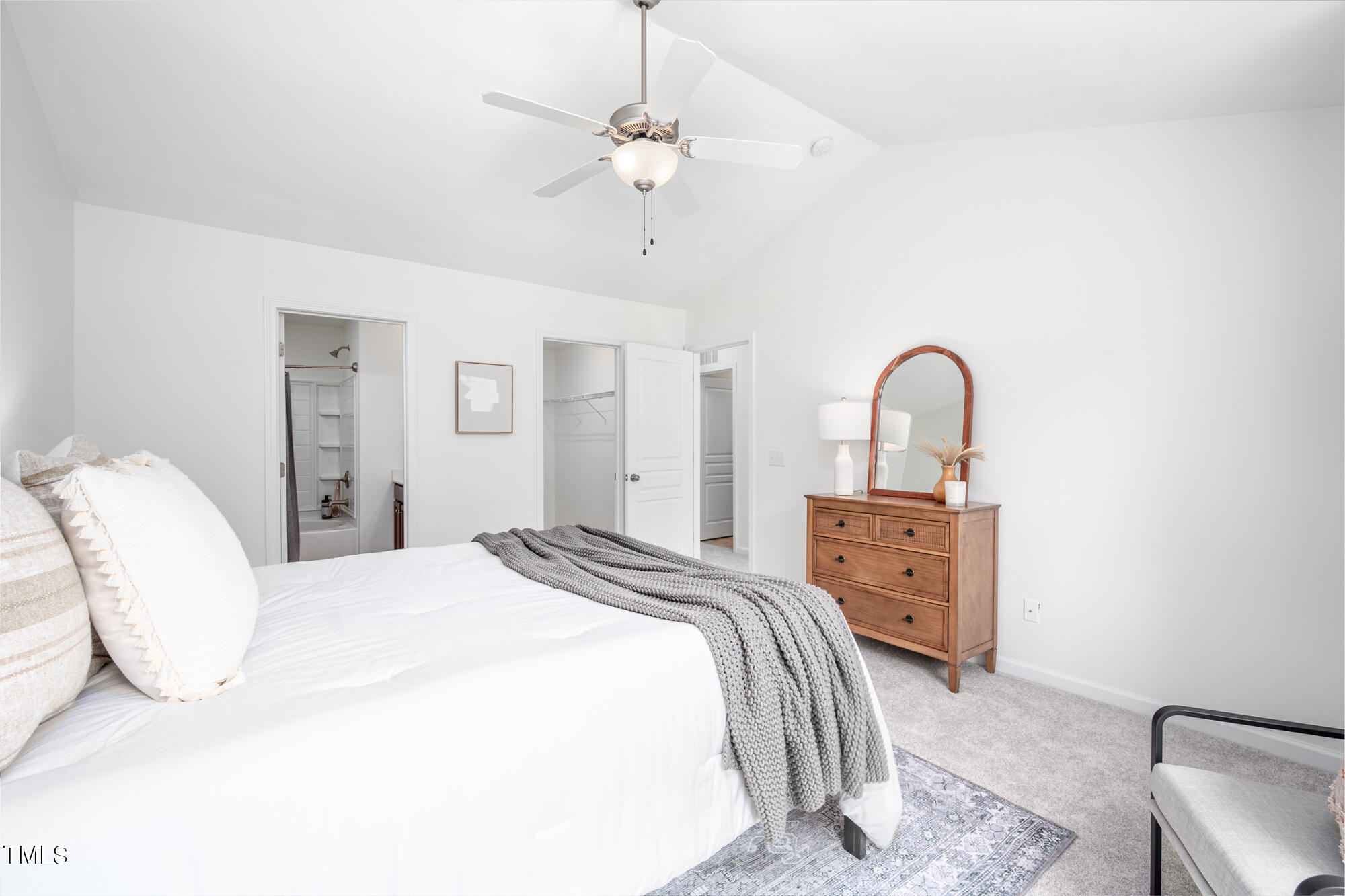 Staged bedroom with a white bed, gray throw, wooden dresser, and arched mirror.