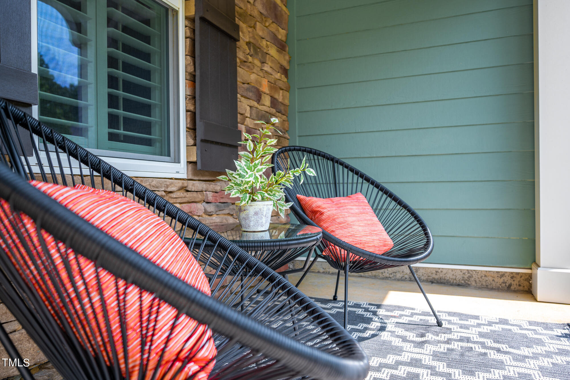 Front porch seating with black woven chairs, coral striped cushions, and a potted plant.