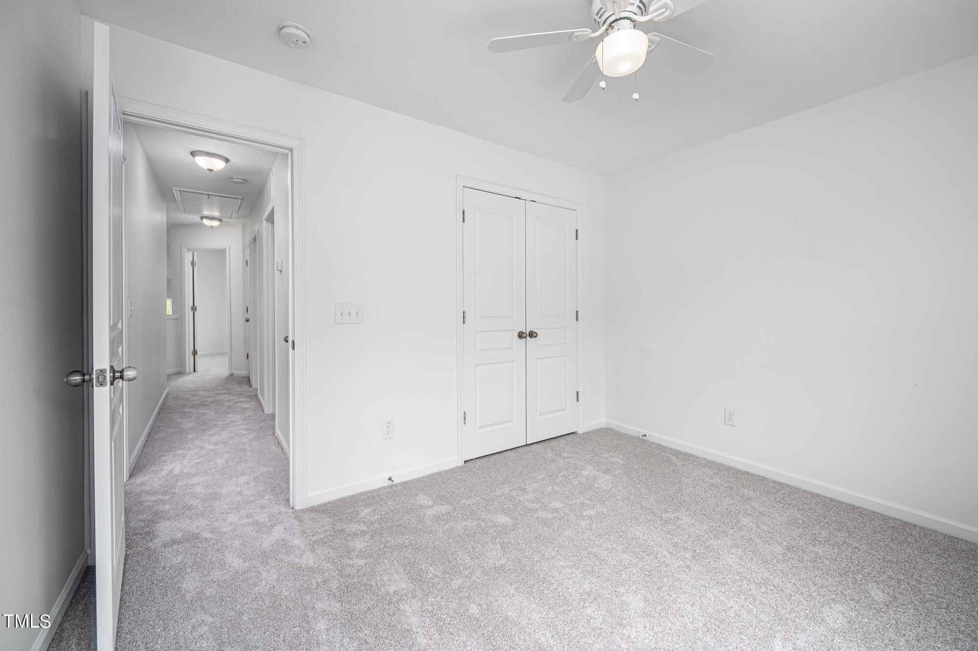 Empty carpeted bedroom with a ceiling fan, double closet doors, and an open doorway to the hall.