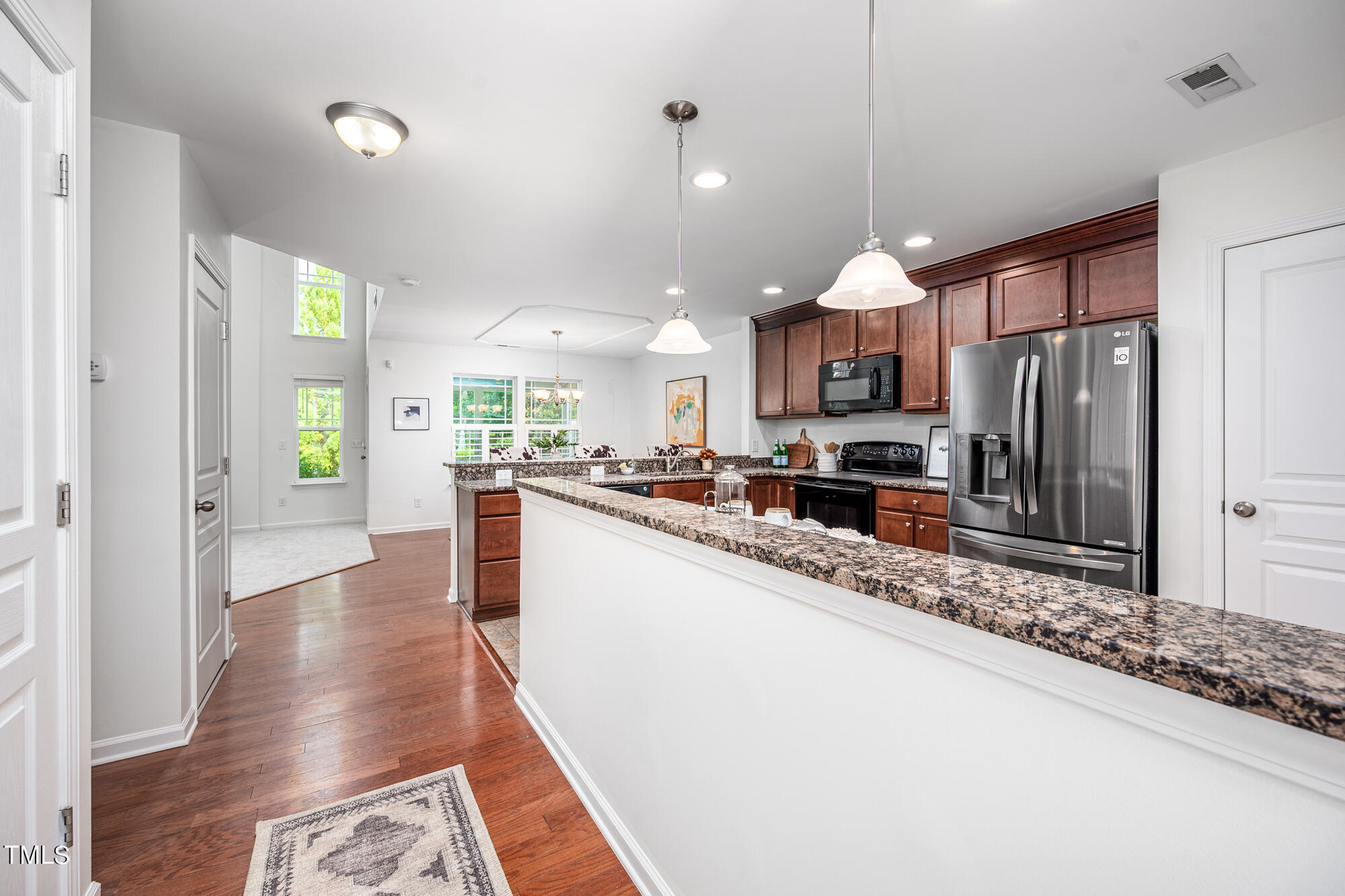Open kitchen with dark wood cabinets, stainless steel appliances, and a long granite breakfast bar.
