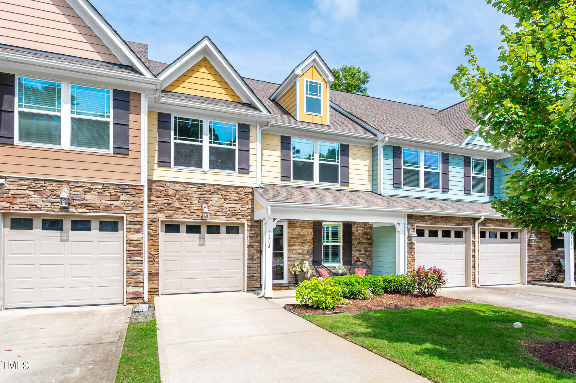 Townhouse exterior with stone veneer, colorful siding, multiple garage doors, and a covered porch.
