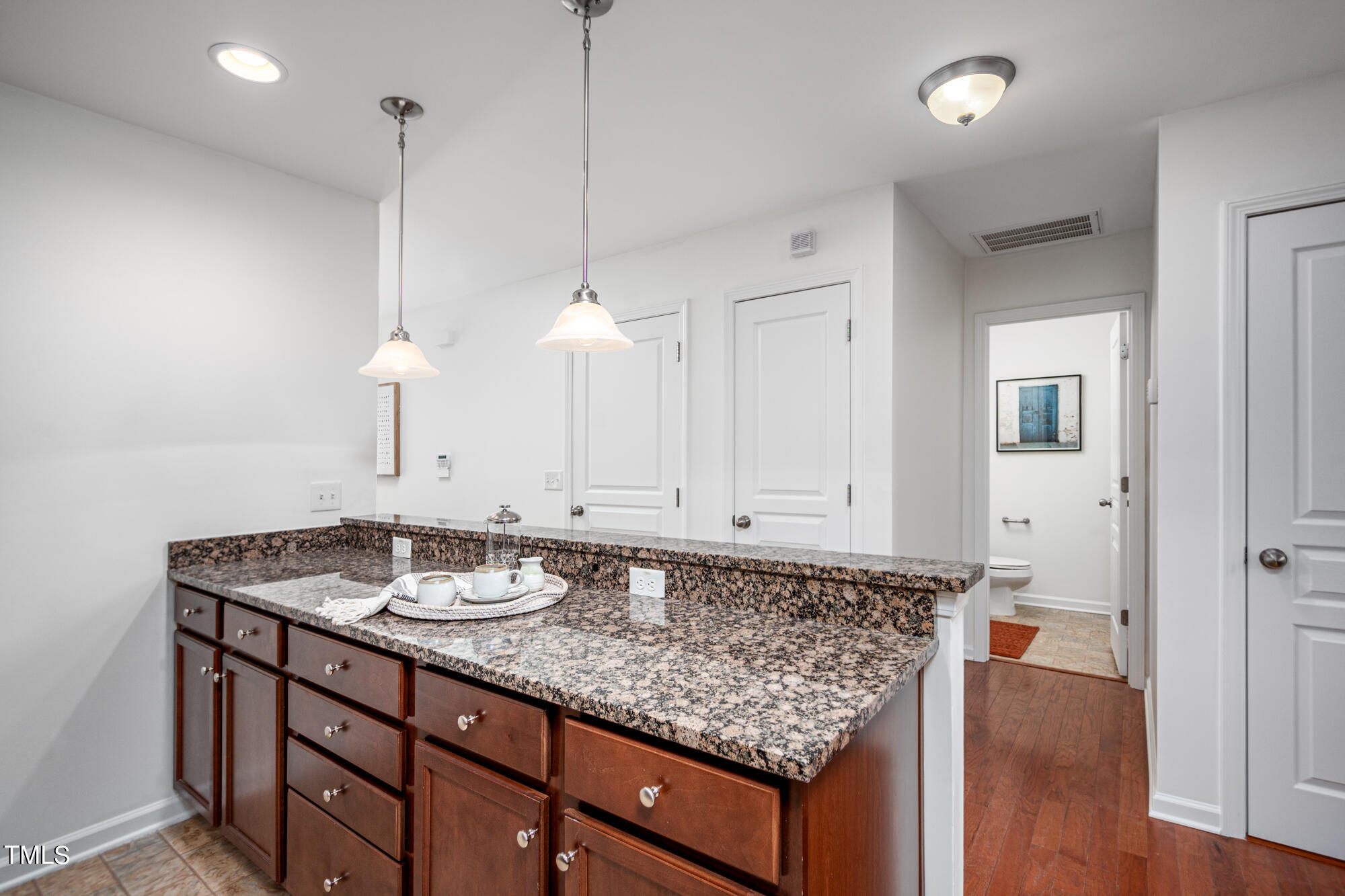 Bathroom vanity with dark wood cabinetry, granite countertop, and pendant lights beside the toilet room.