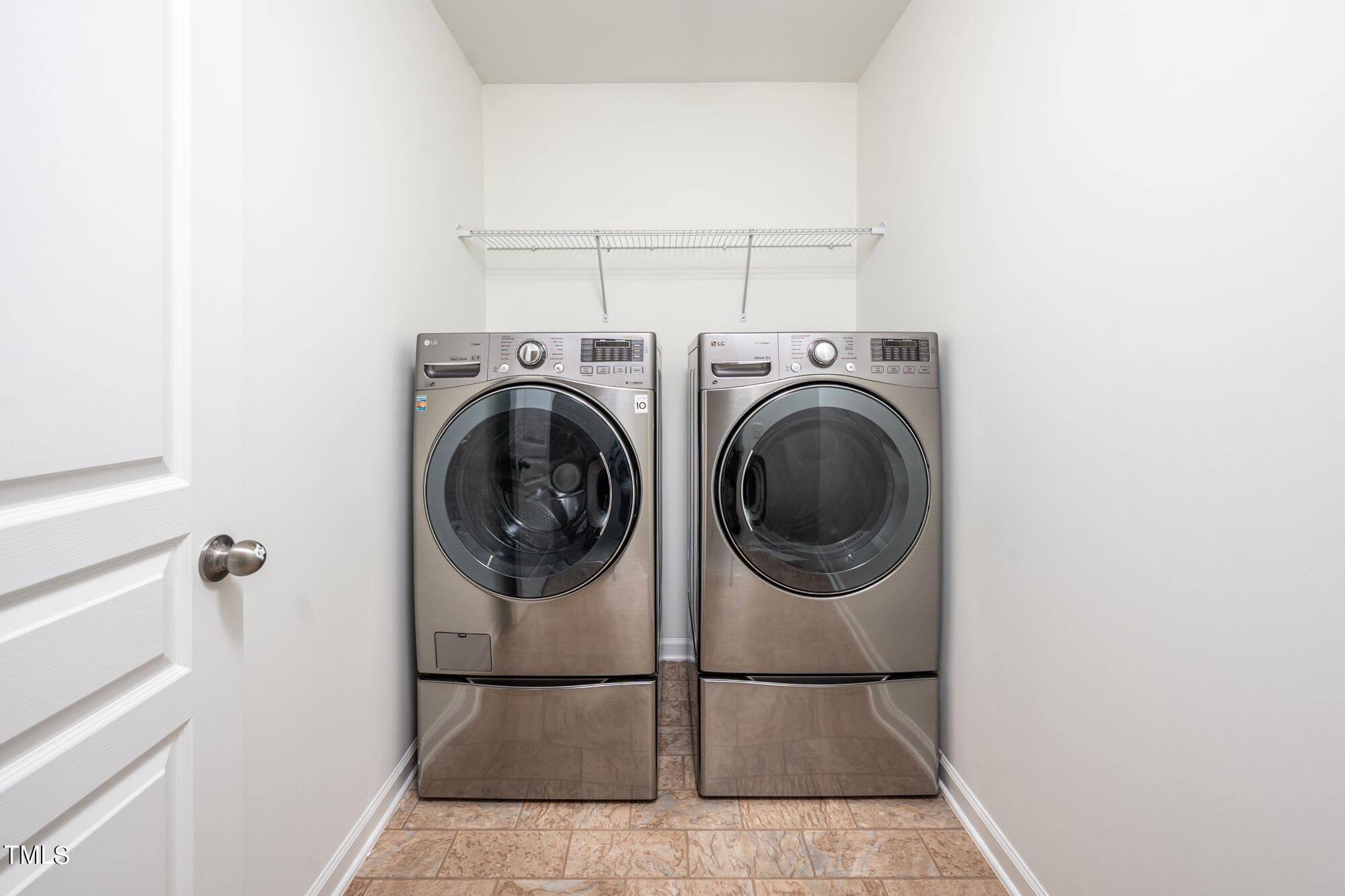 Laundry room with matching stainless-steel front-loading washer and dryer beneath a wire shelf.