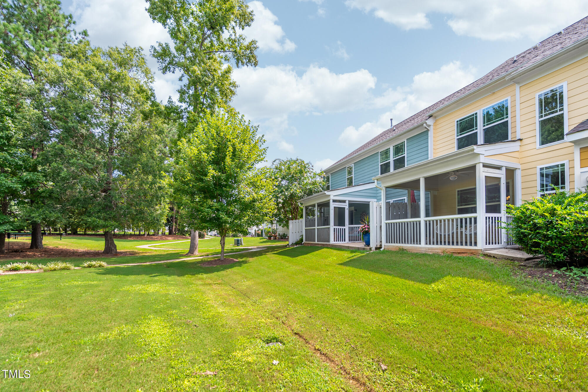 Two-story home with screened porches facing a spacious lawn and mature trees.