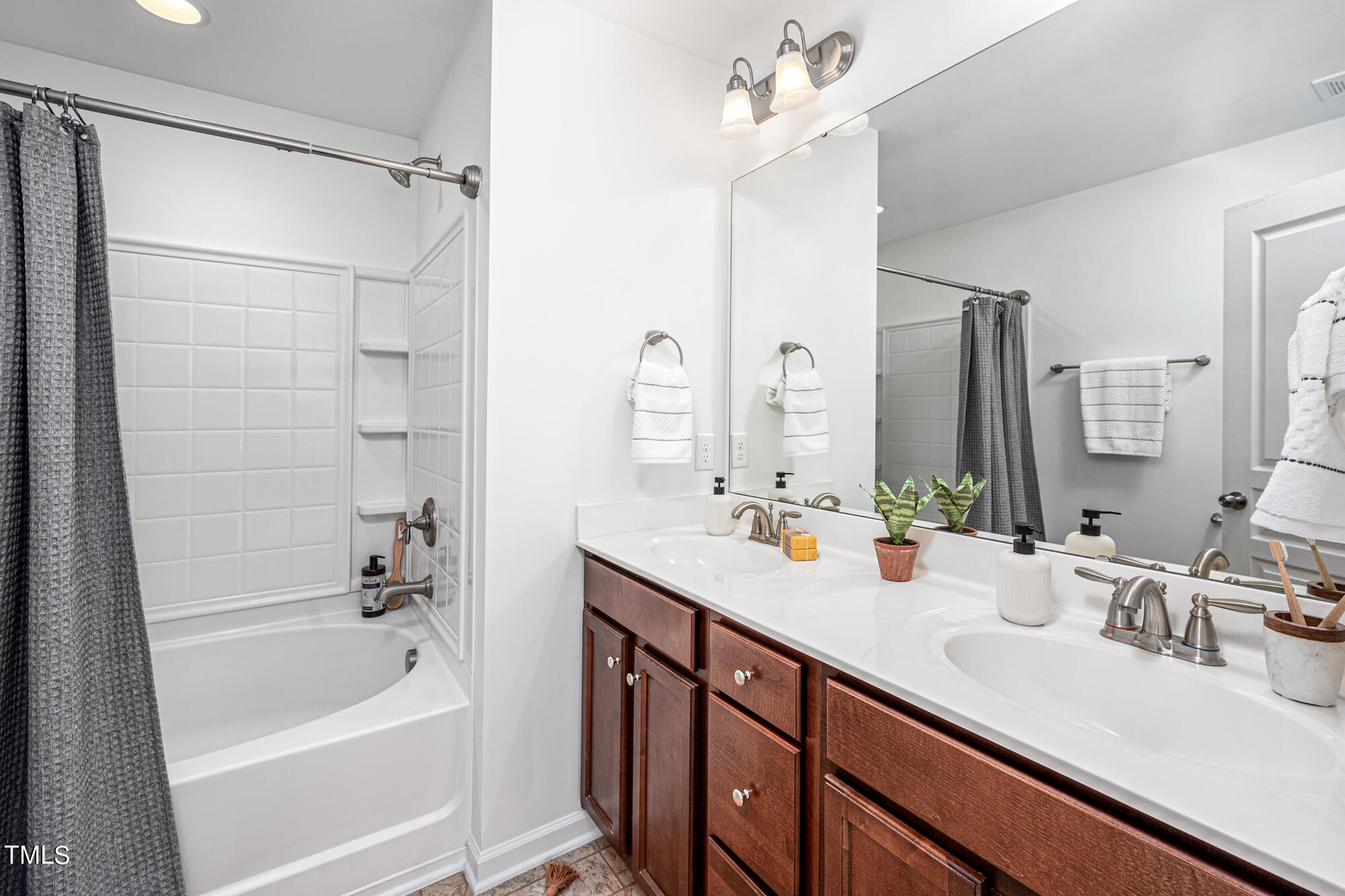 Bathroom with double-sink vanity, dark wood cabinets, and a tub-shower behind a gray curtain.