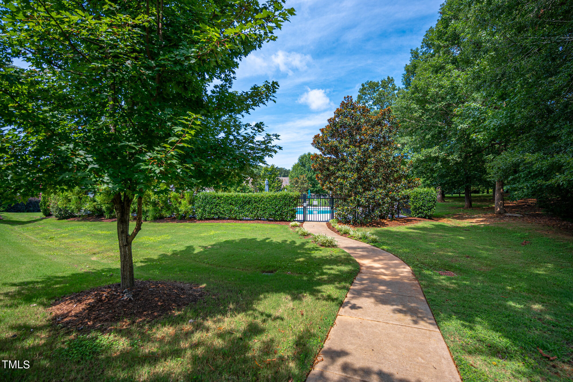 Curved walkway leads through a tree-shaded lawn to a fenced swimming pool.