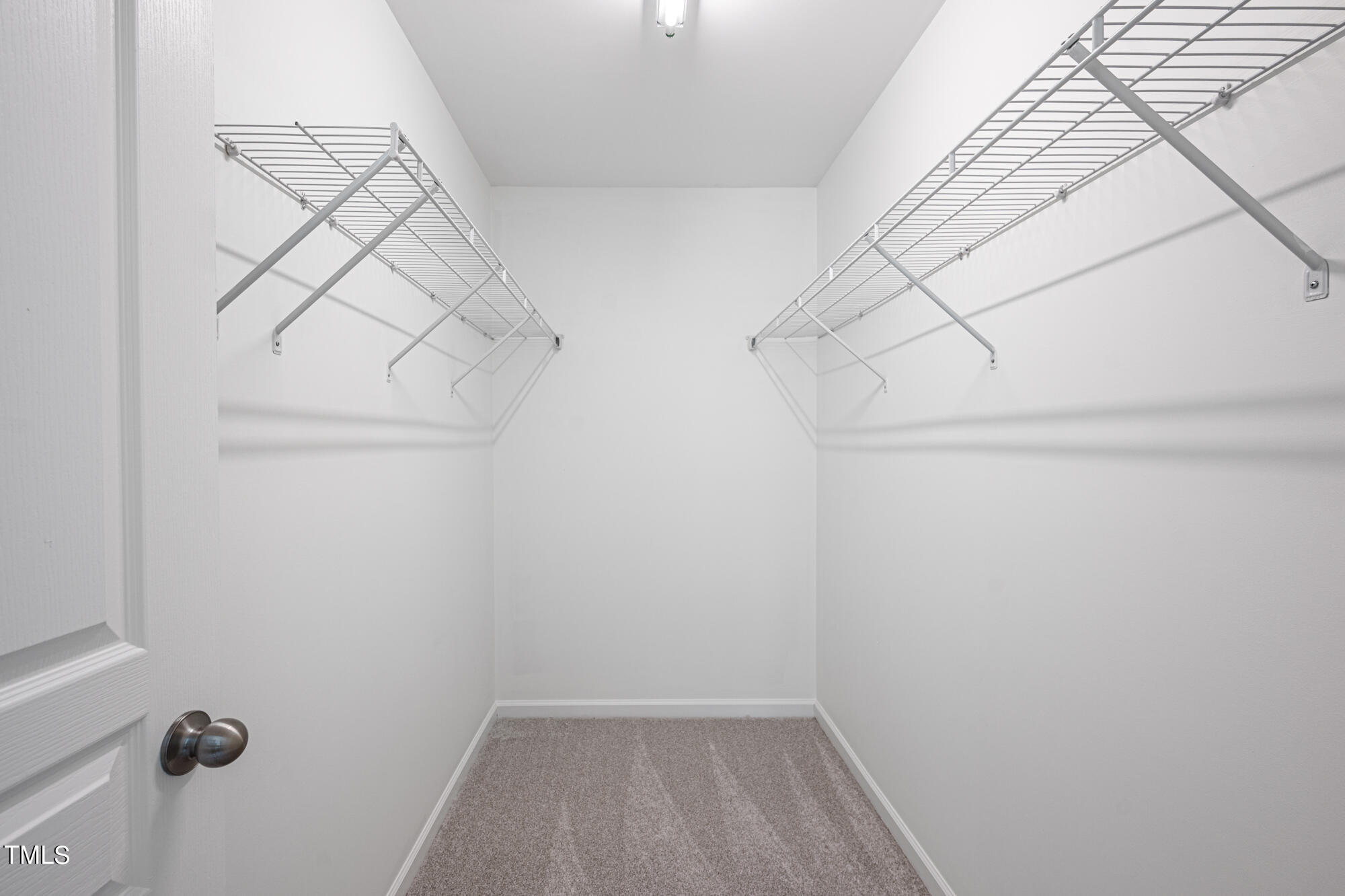 Empty walk-in closet with wire shelving along both walls and beige carpet.