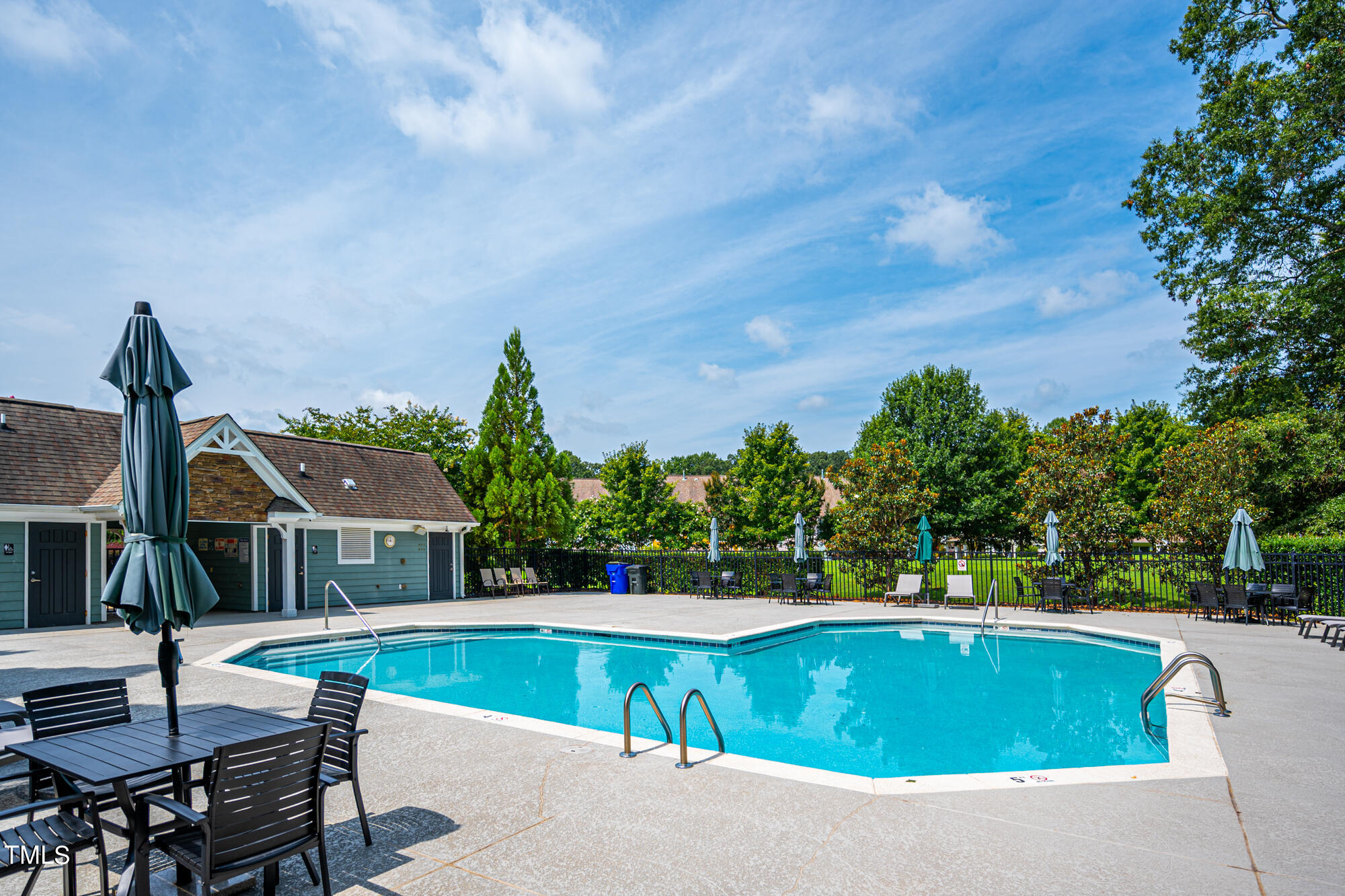 Outdoor swimming pool with a paved deck, seating, closed umbrellas, and a small building.