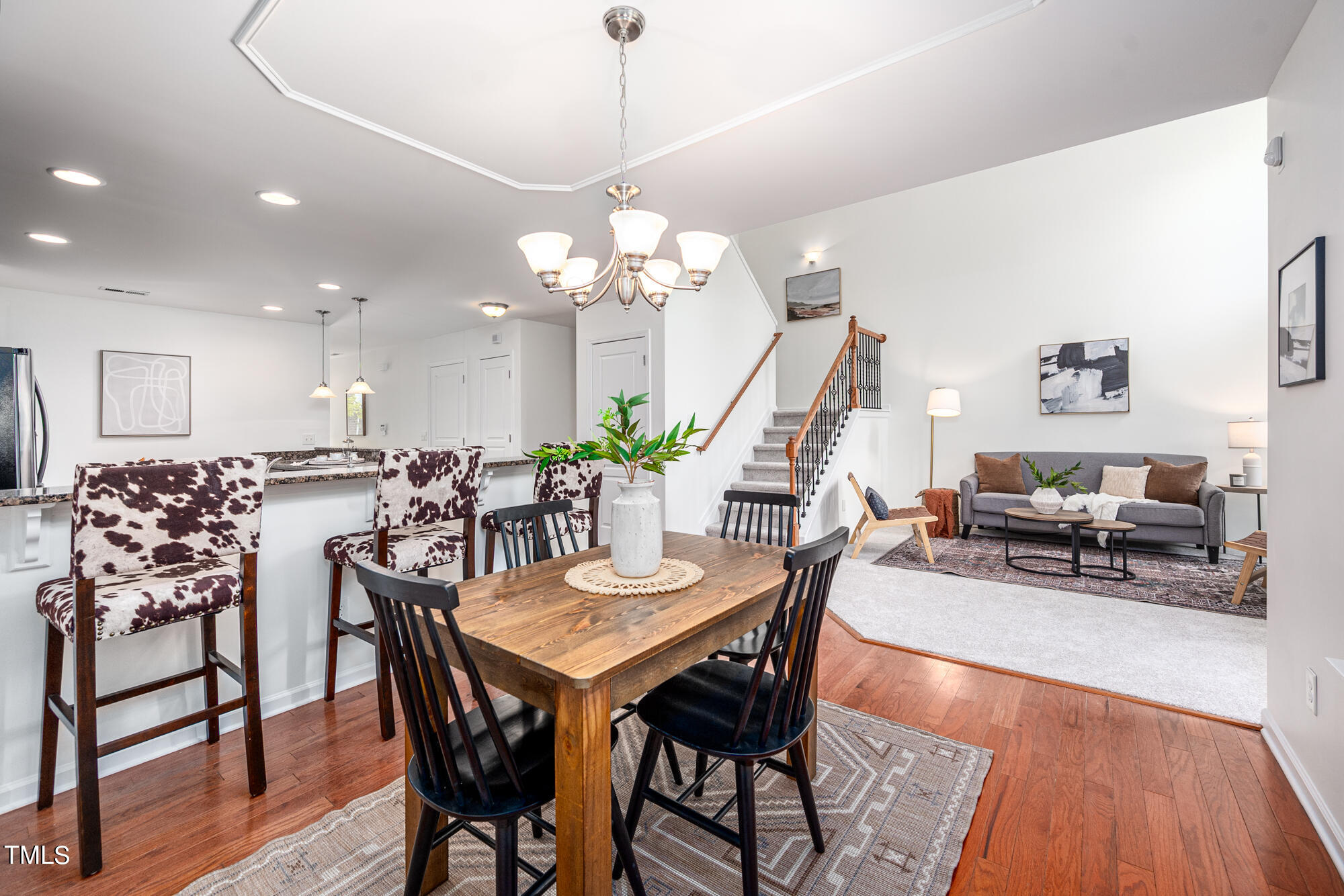 Open dining and living area with a wood table, cow-print stools, gray sofa, and staircase.