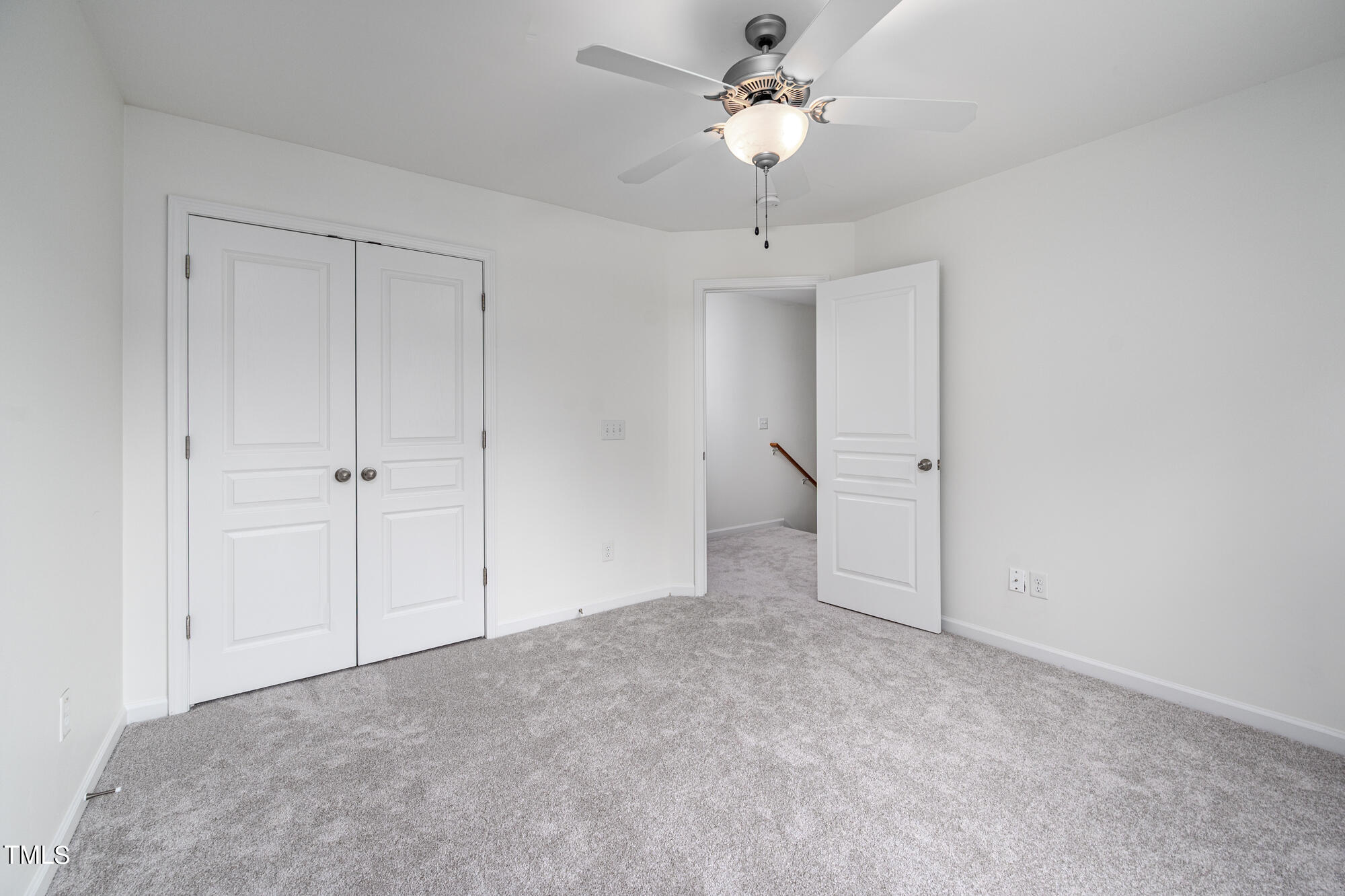 Empty bedroom with gray carpet, double closet doors, and a ceiling fan with light.