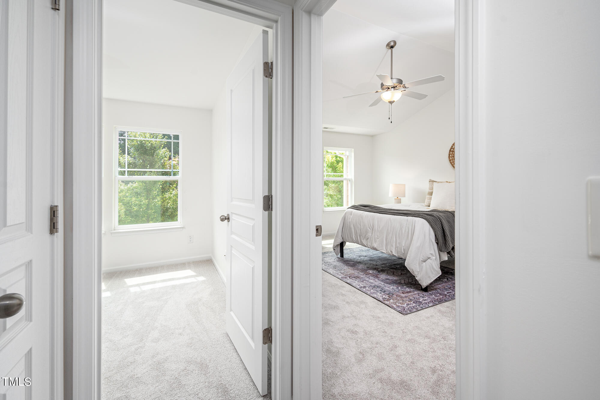 Bedroom with a white bed and patterned rug, seen through adjoining bright rooms.