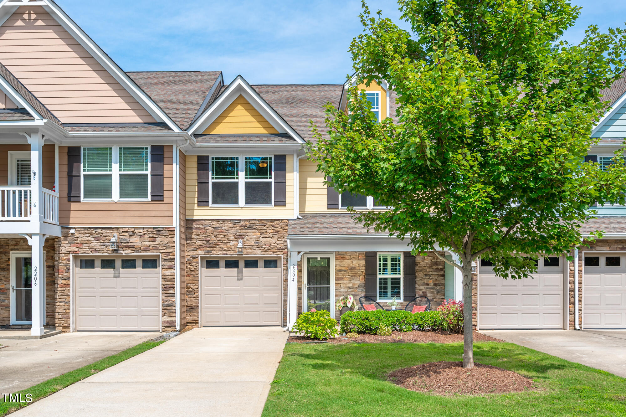 Home numbered 2204 with yellow siding, a stone facade, attached garage, and leafy front-yard tree.