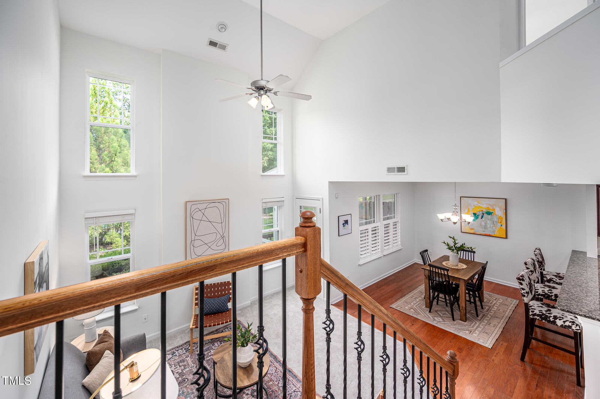 Two-story living and dining area with tall windows, hardwood floors, and a wood-and-iron stair railing.