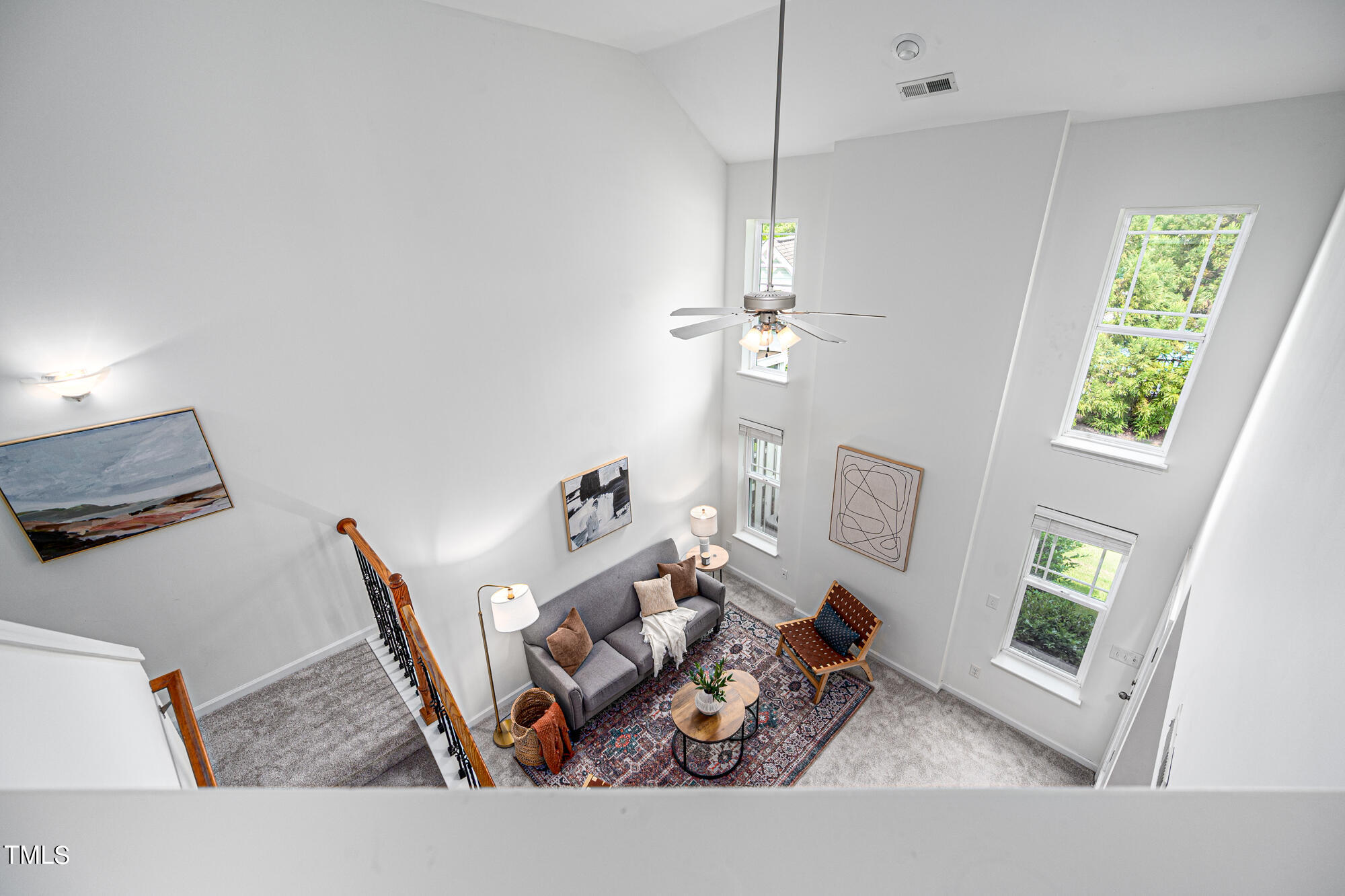 Double-height living room with a gray sofa, patterned rug, tall windows, and ceiling fan.