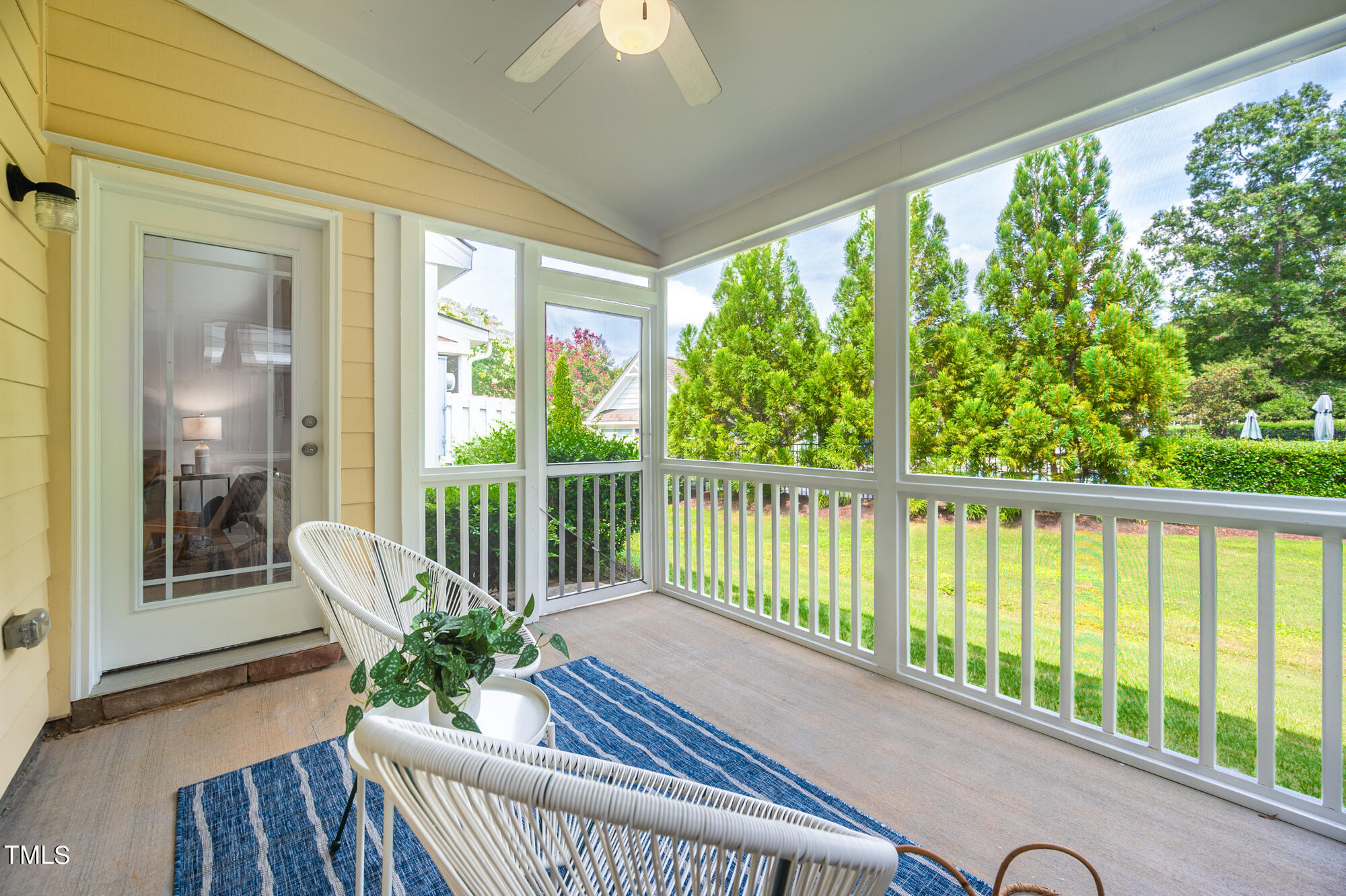 Screened porch with wicker chairs and a blue rug overlooking a green lawn and trees.