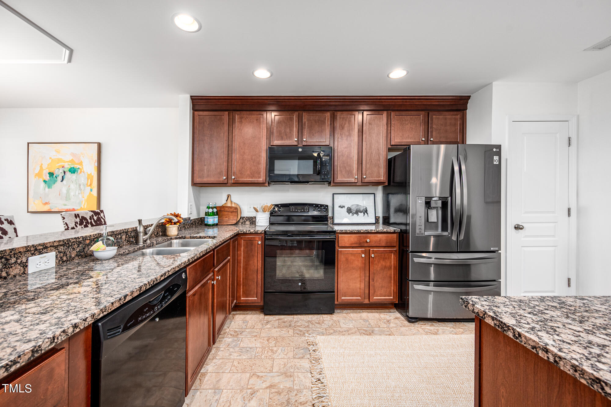 Kitchen with cherry cabinets, granite counters, stainless steel refrigerator, and black range.