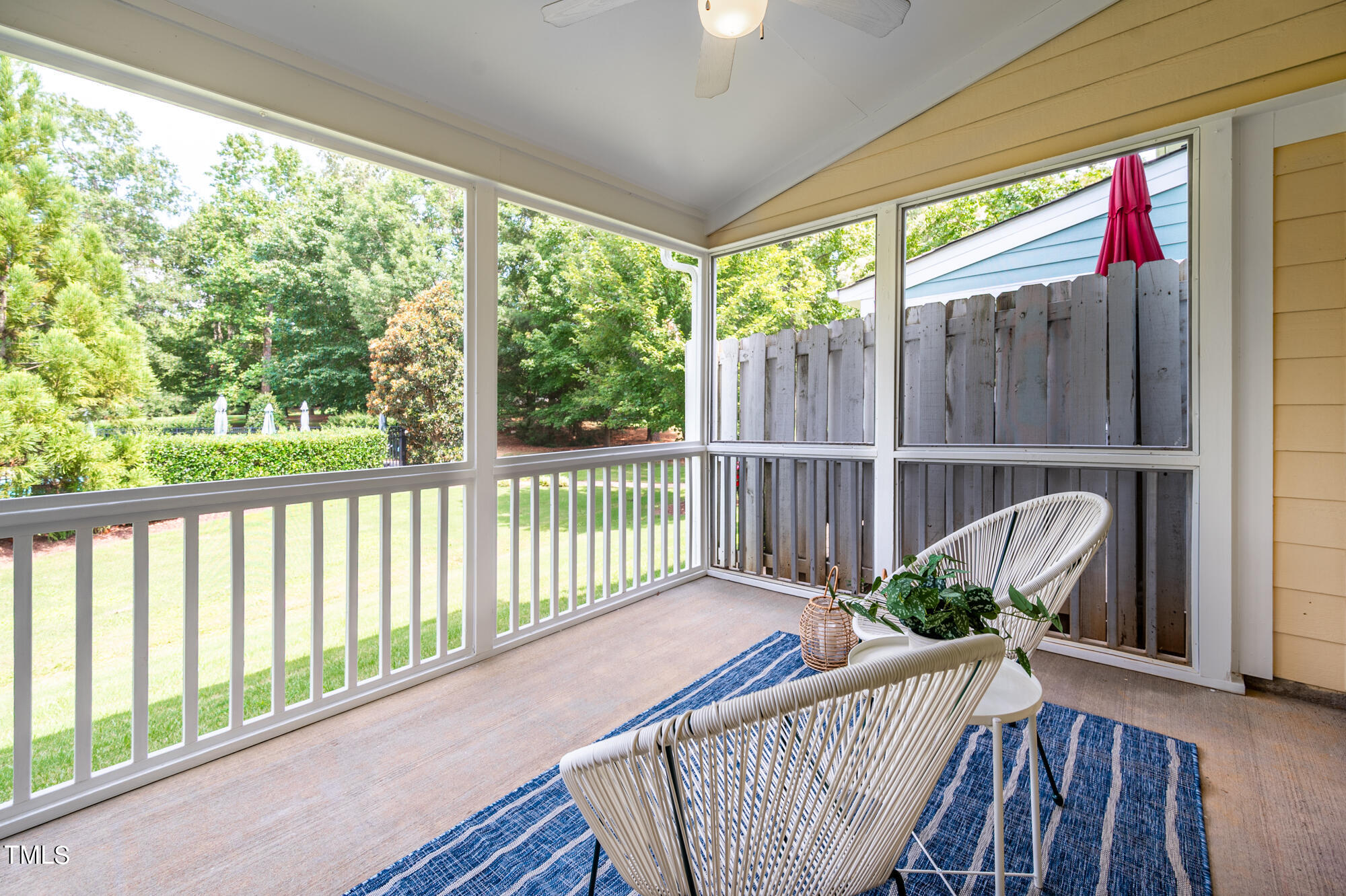 Screened porch with white wicker seating, a blue striped rug, and views of the lawn and trees.