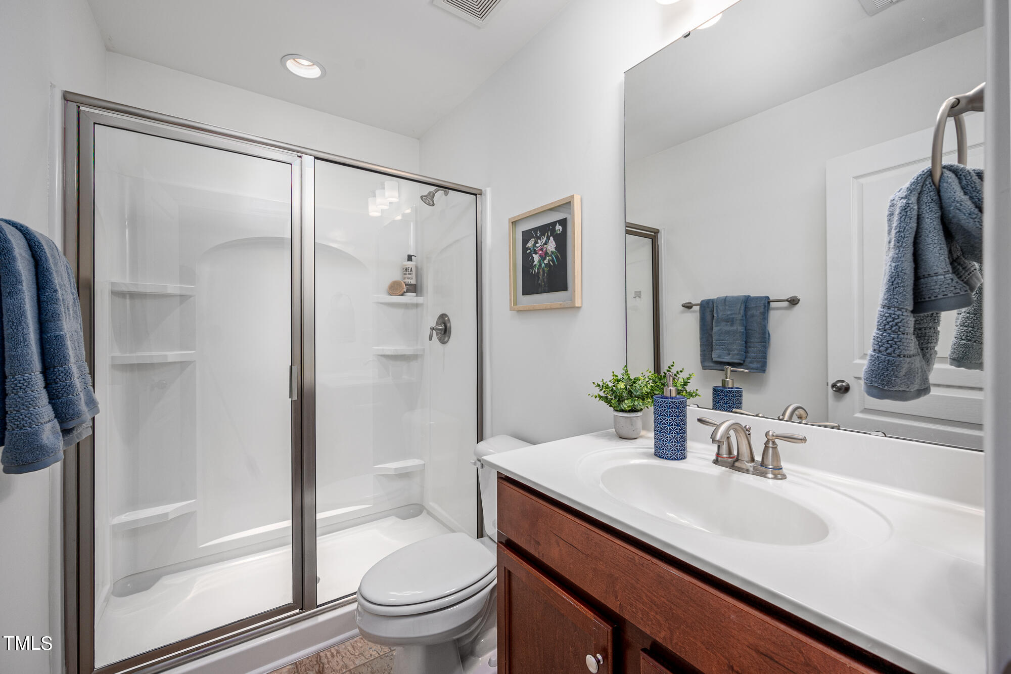 Bathroom with glass shower, white sink counter, dark wood vanity, and blue towels.