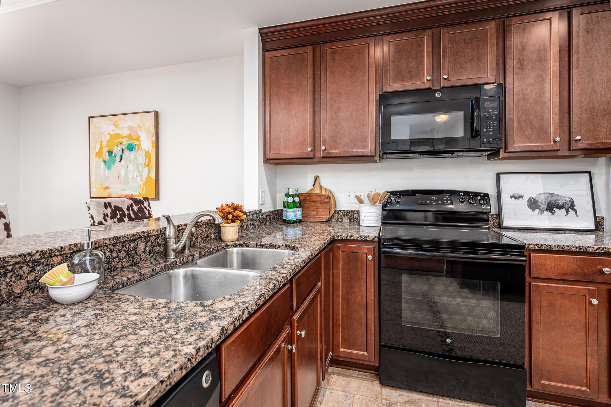 Kitchen with reddish-brown cabinets, speckled granite counters, a double sink, and black appliances.