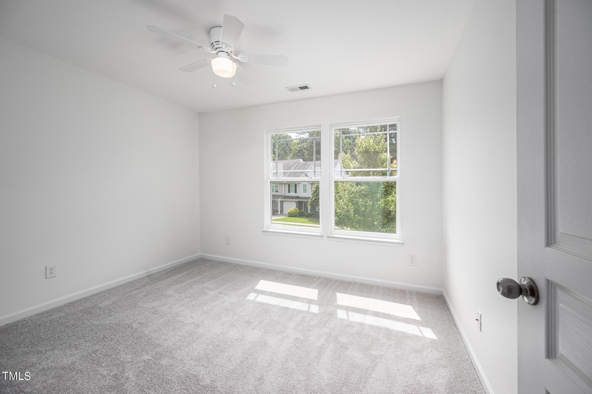Empty bedroom with gray carpet, a ceiling fan, and two sunlit windows.