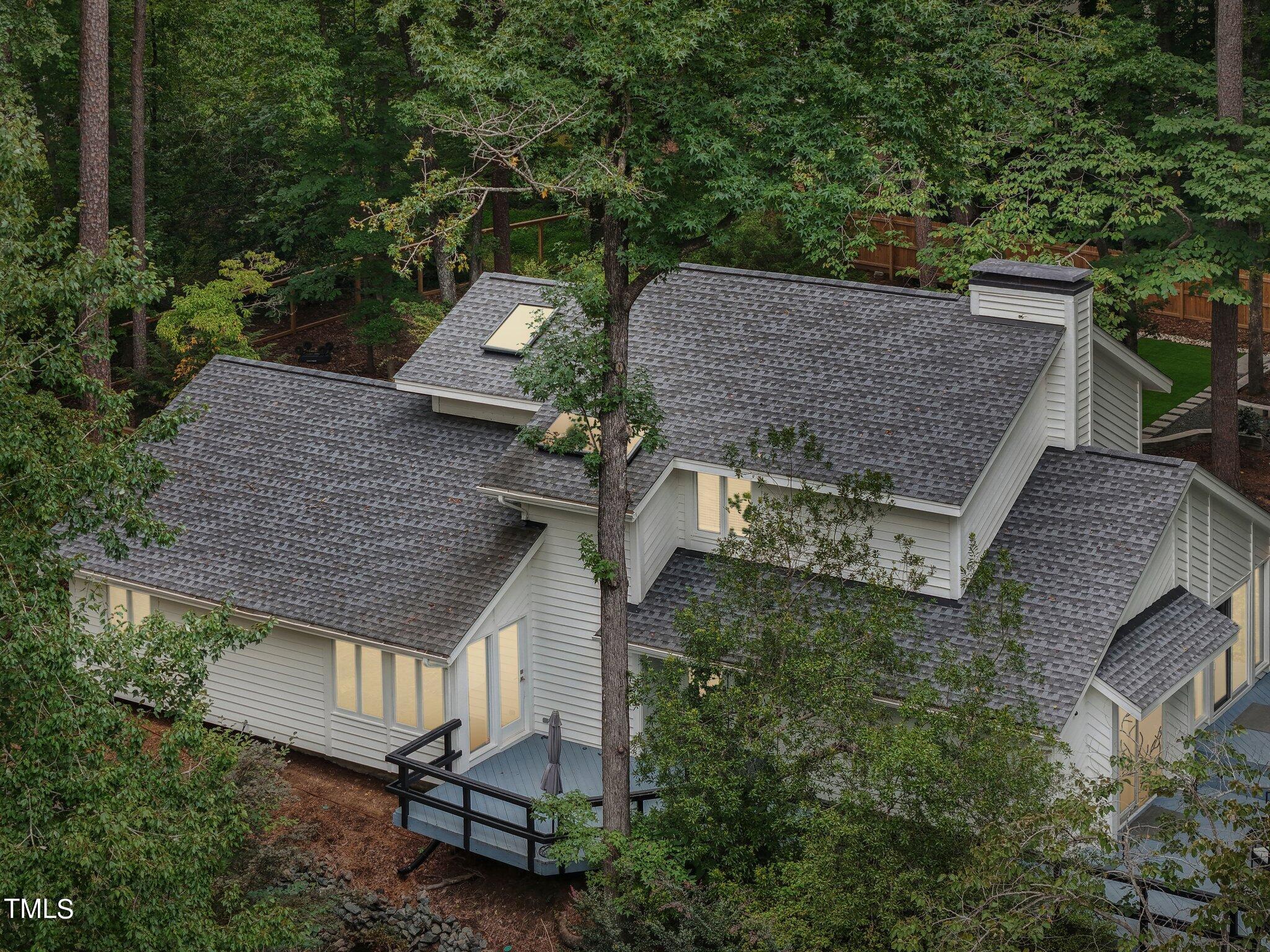 Aerial view of a white-sided house among mature trees, with skylights and a deck.