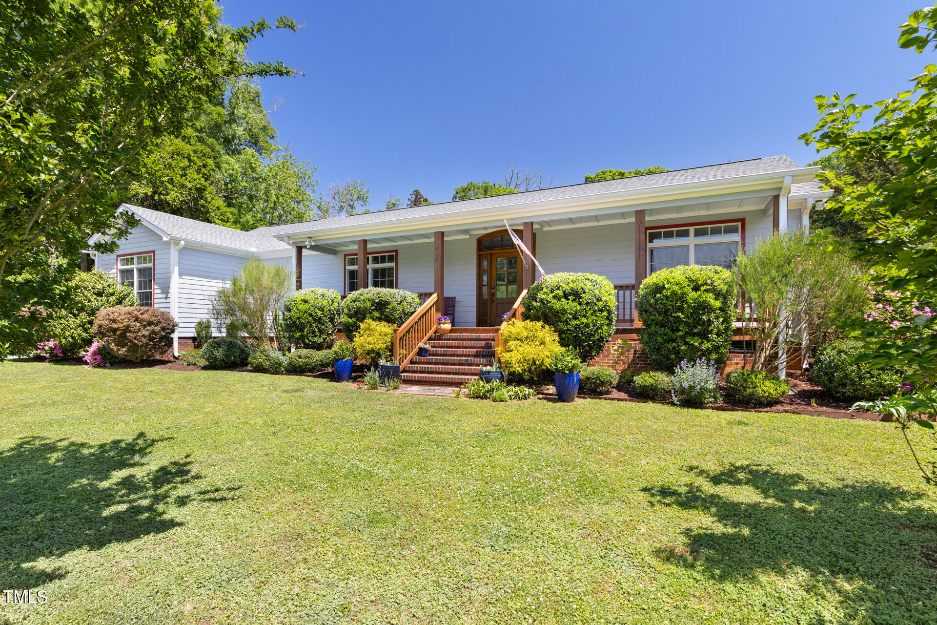White single-story home with a covered porch, brick steps, and landscaped front lawn.
