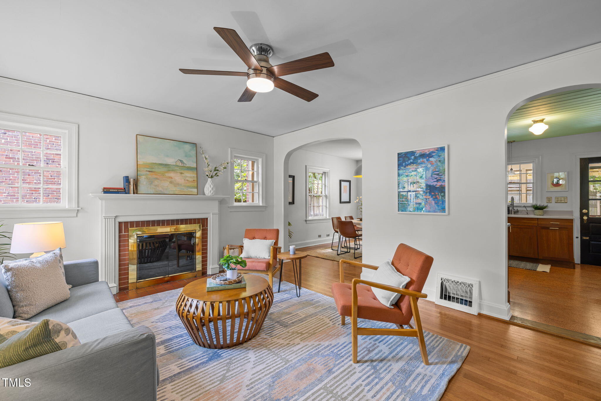 Living room with a brick fireplace, wood ceiling fan, and arched openings to the dining area and kitchen.