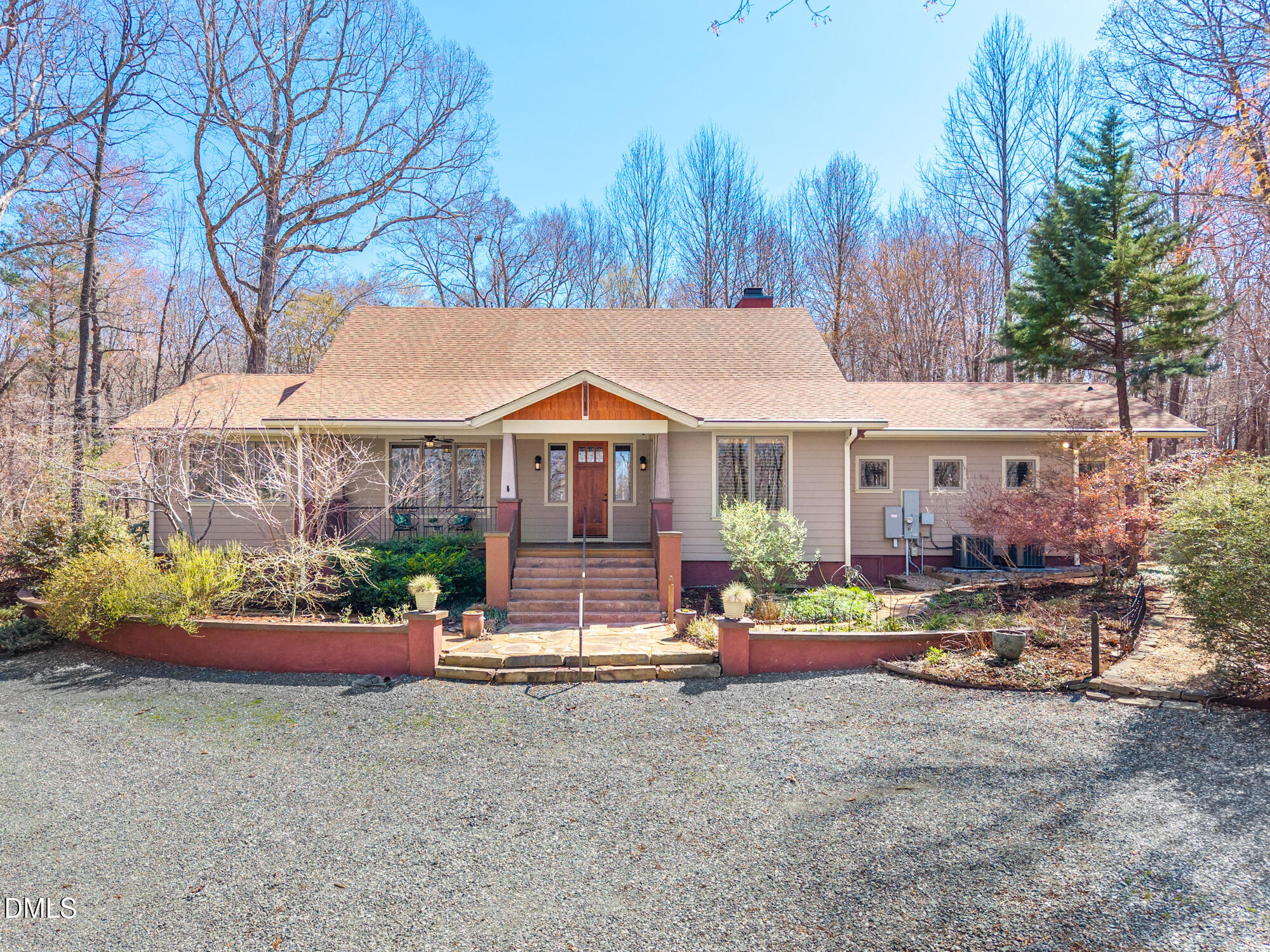 Single-story home with a central covered entry, gravel driveway, and leafless trees.