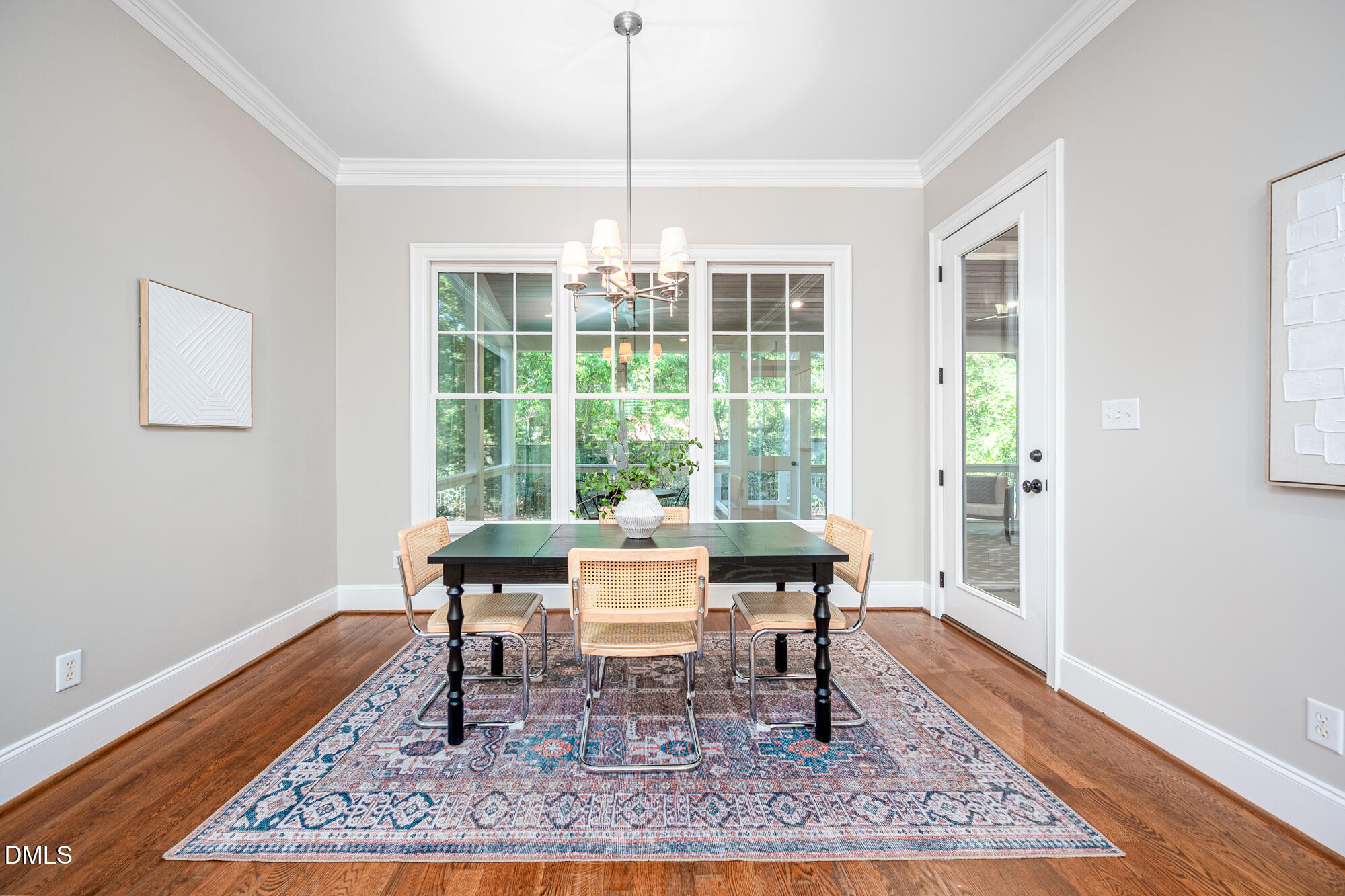 Dining room with a dark table, cane-back chairs, patterned rug, and large windows overlooking greenery.