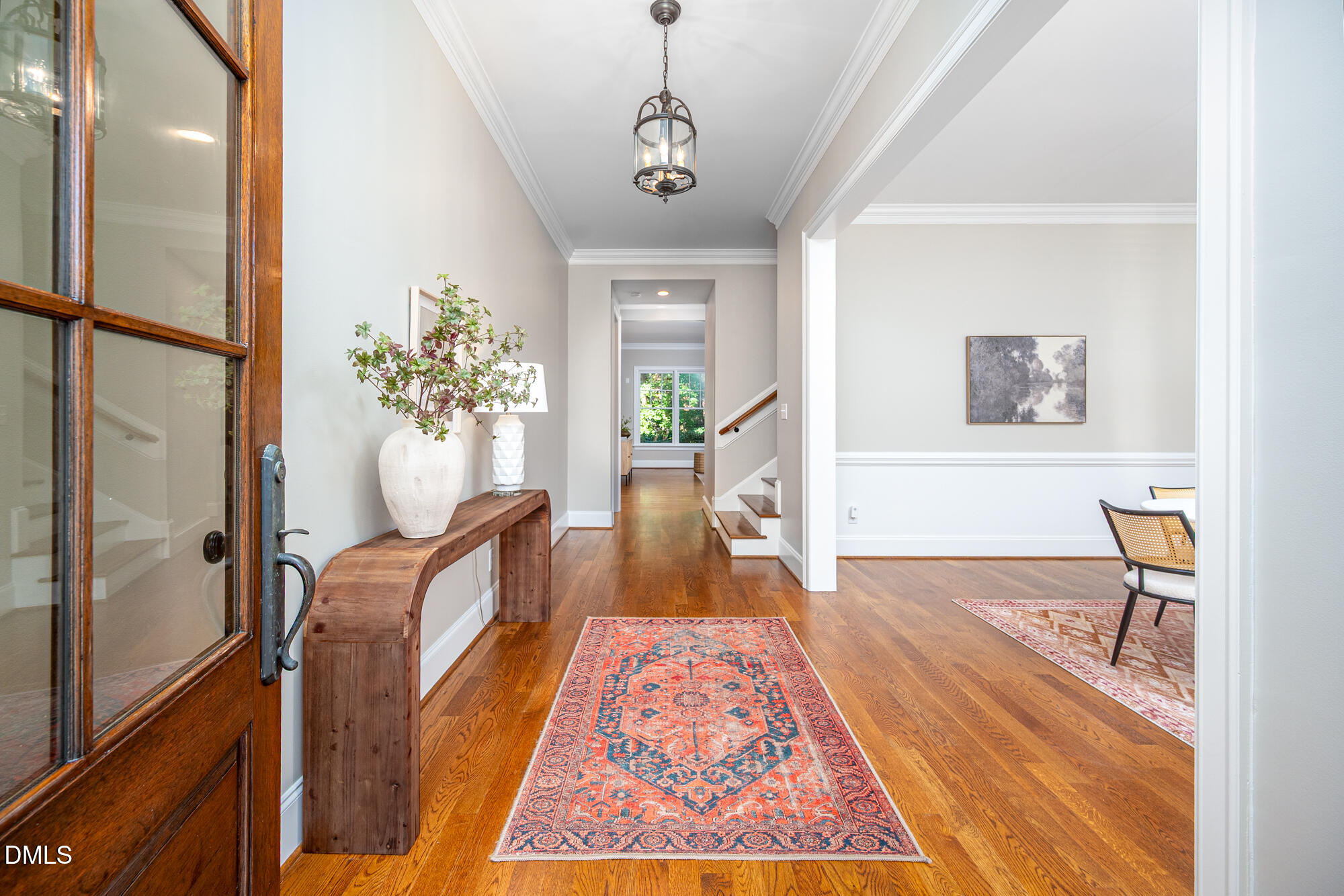 Entry foyer with hardwood floors, a patterned runner, and a wood console beside the glass-paneled front door.
