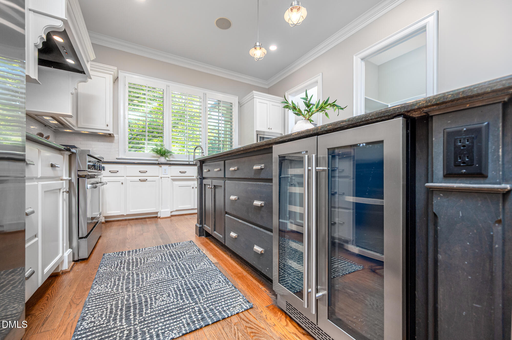 Kitchen with white cabinets, dark island, glass-front beverage refrigerators, and plantation-shuttered windows.