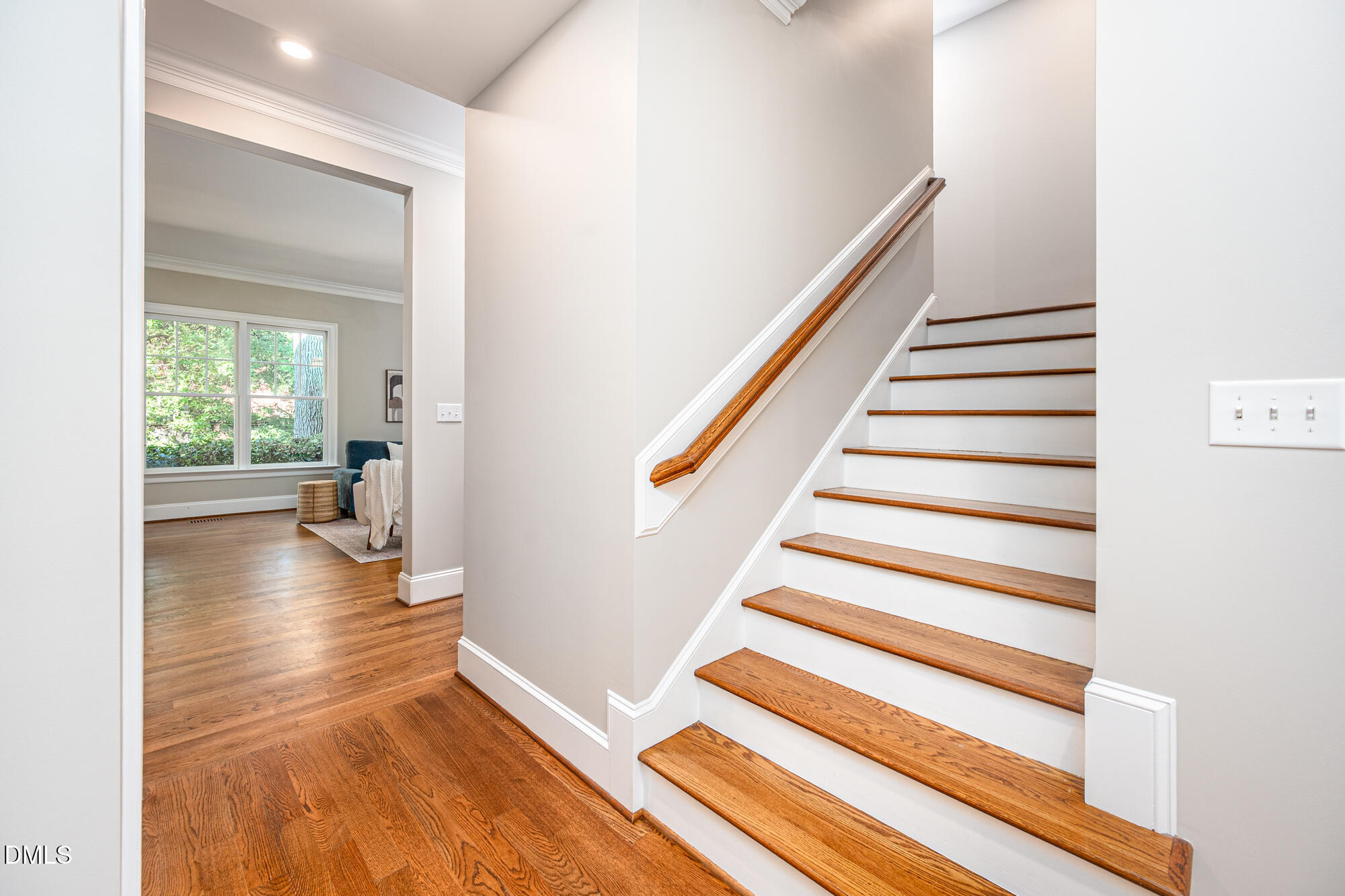 Foyer with a hardwood staircase and polished wood handrail beside a sunlit sitting area.