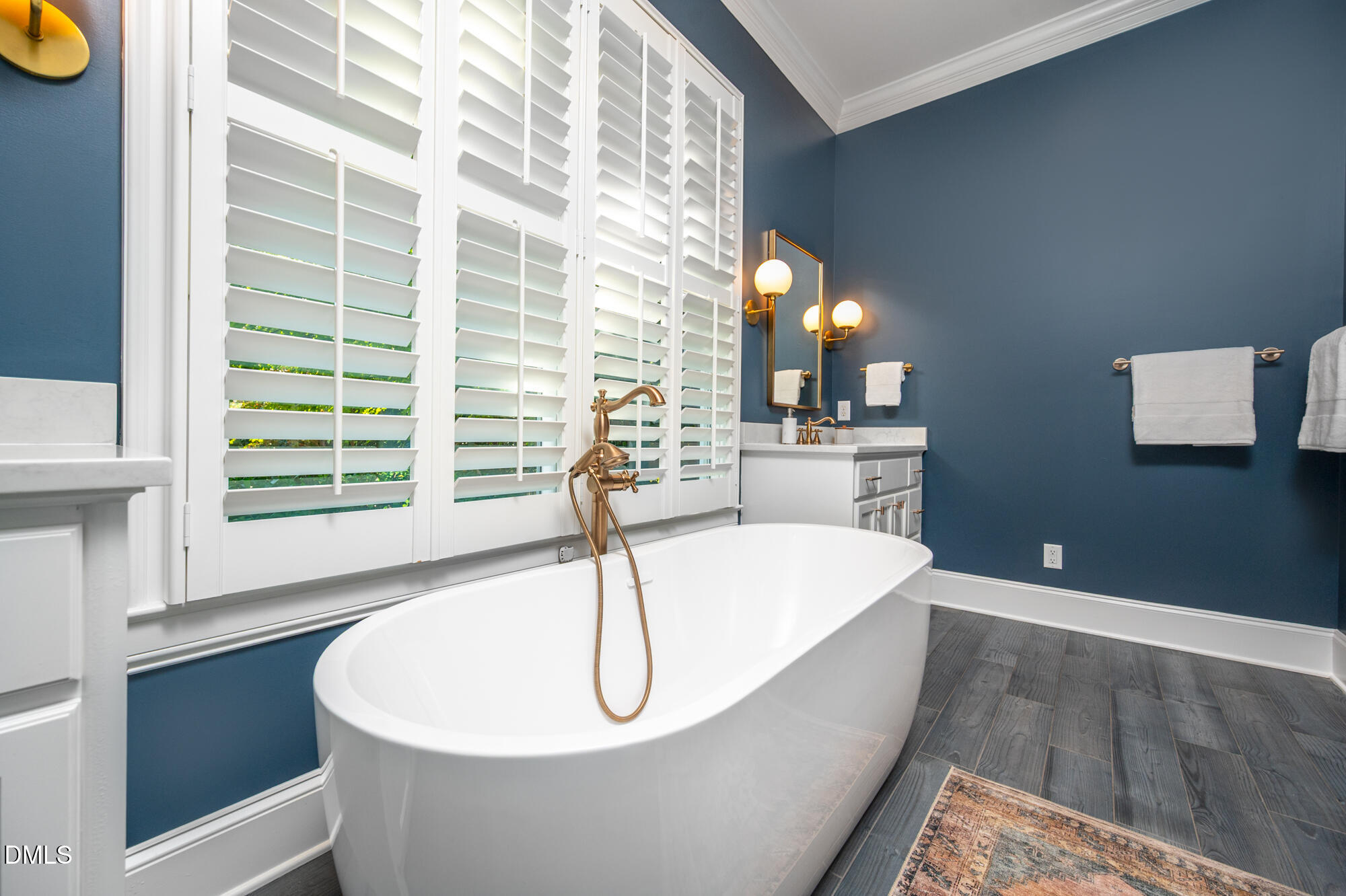 Bathroom with a freestanding tub beneath plantation shutters and brass fixtures against navy-blue walls.