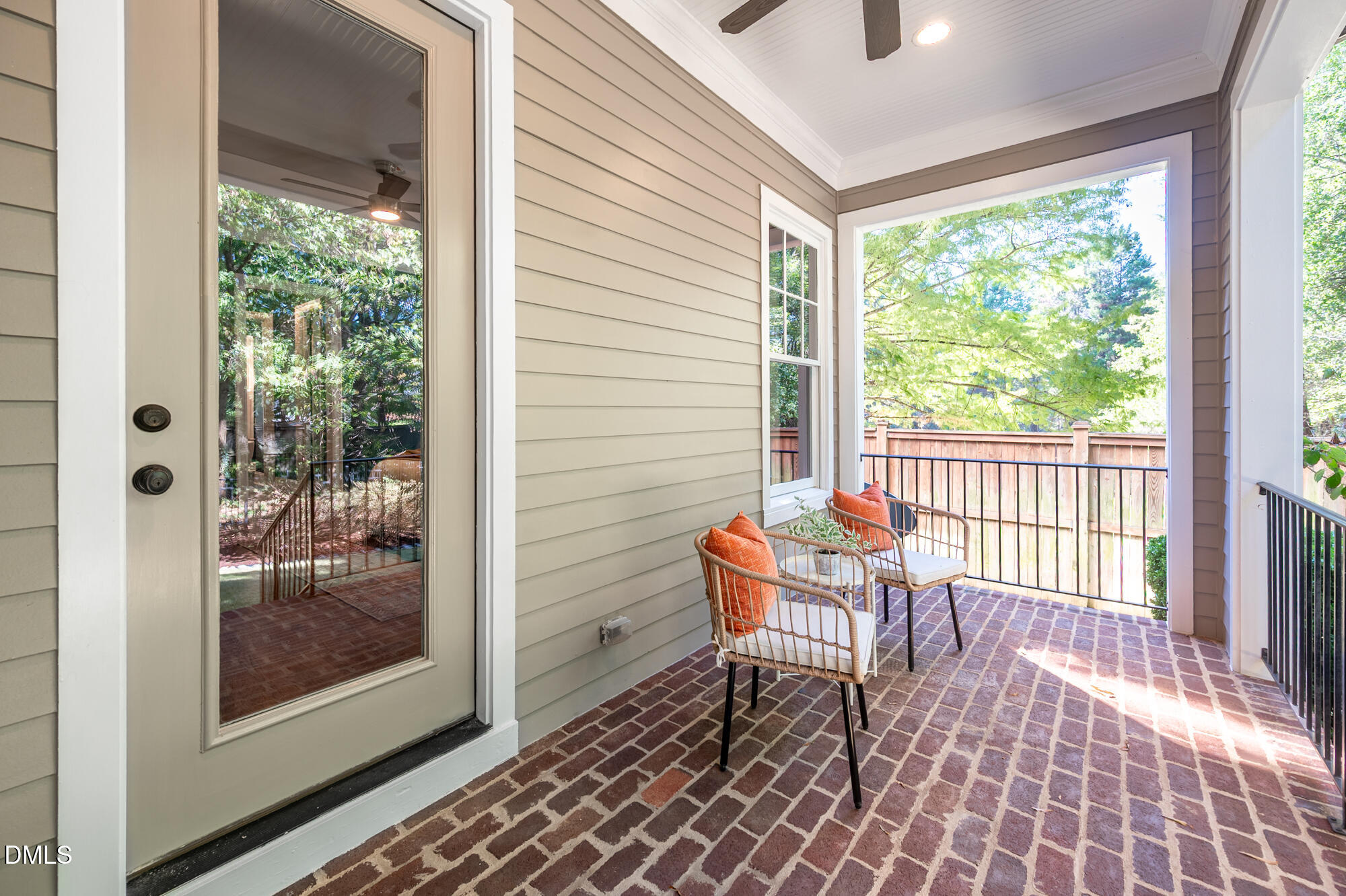 Covered brick porch with two wicker chairs and a leafy wooded view.