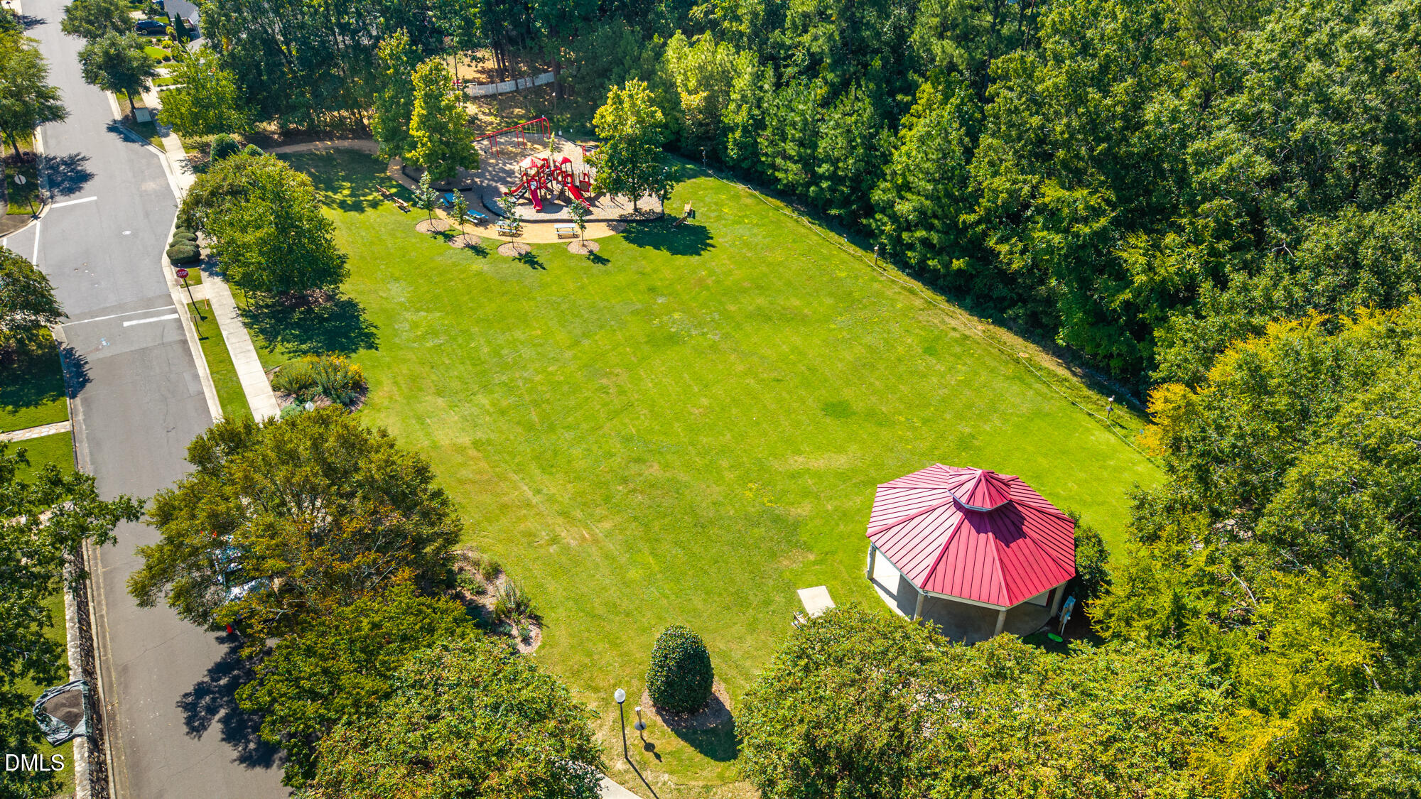 Aerial view of a community lawn with a red playground and pavilion surrounded by trees.