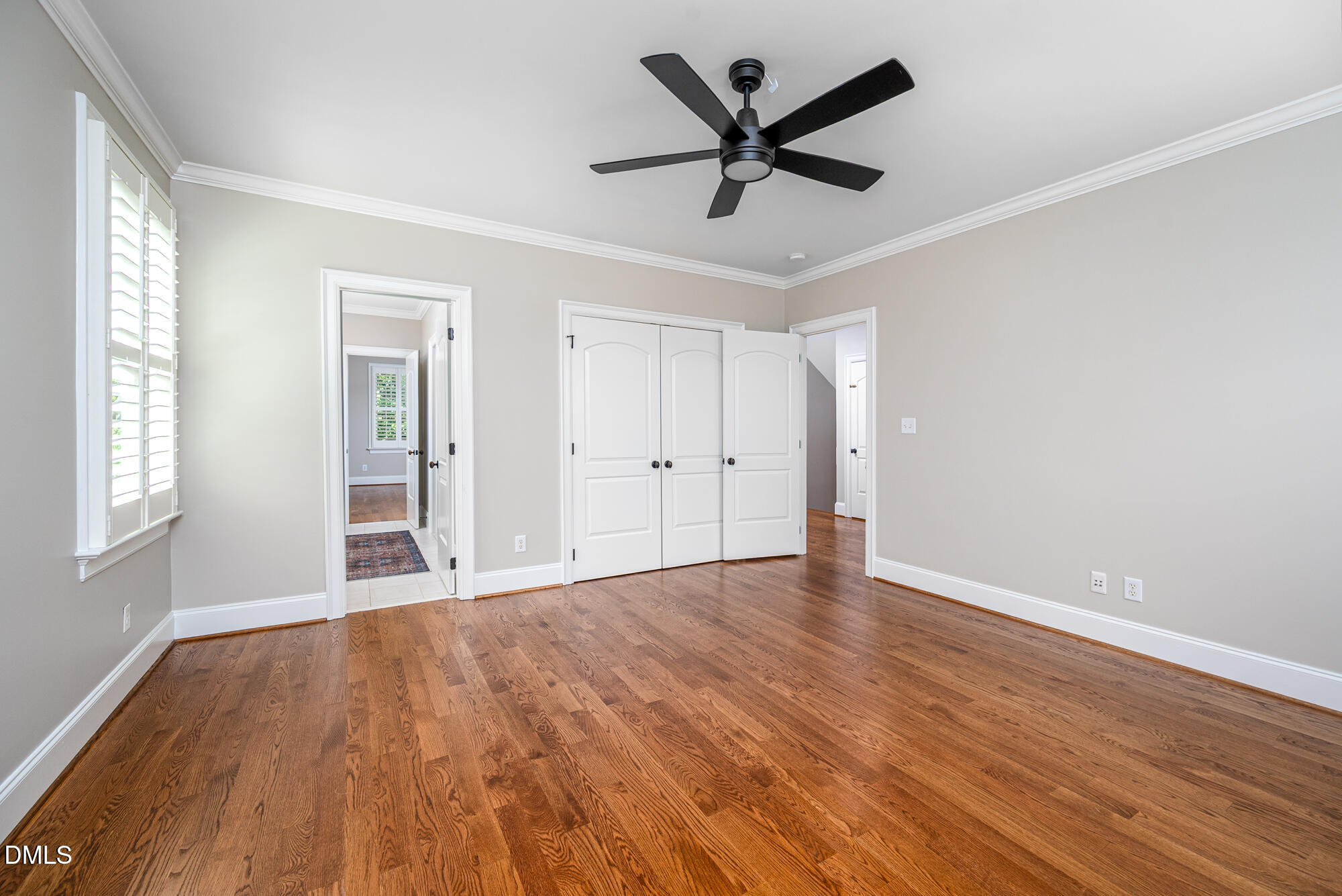 Empty bedroom with hardwood floors, plantation shutters, and a black ceiling fan.