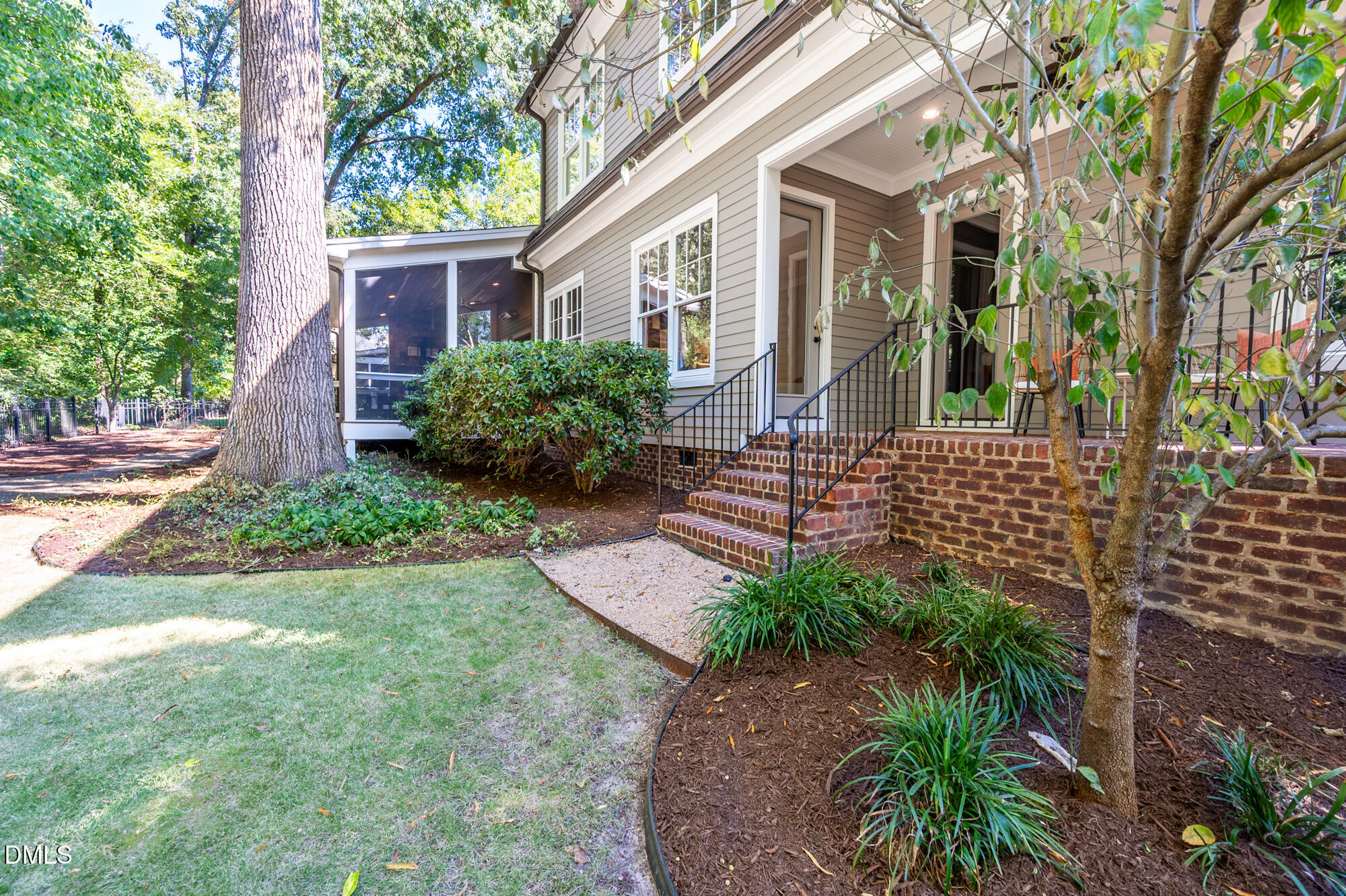 Home exterior with a raised covered entry, brick steps, and screened porch among mature trees.