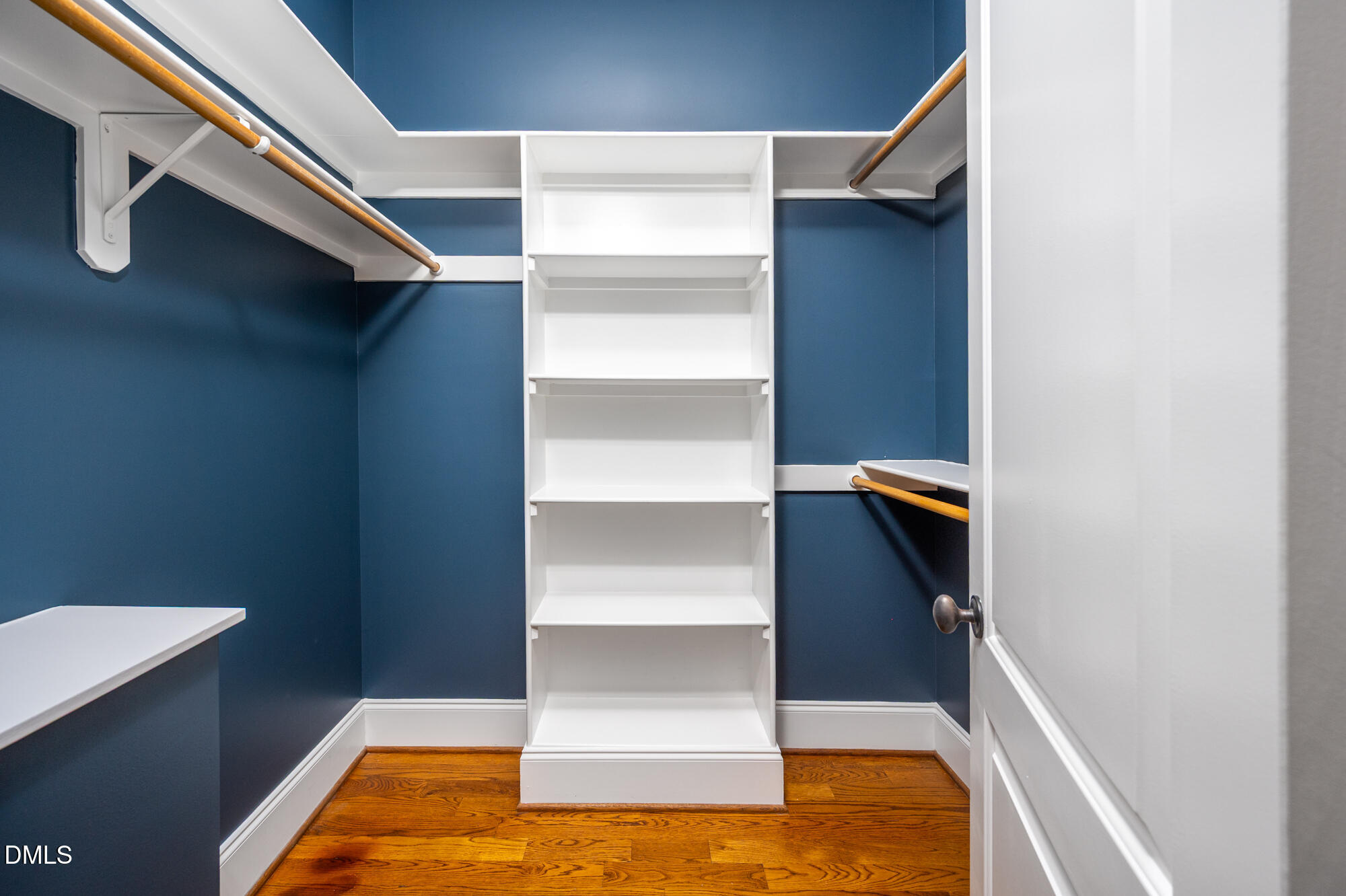 Walk-in closet with white built-in shelving, wooden hanging rods, and blue walls.